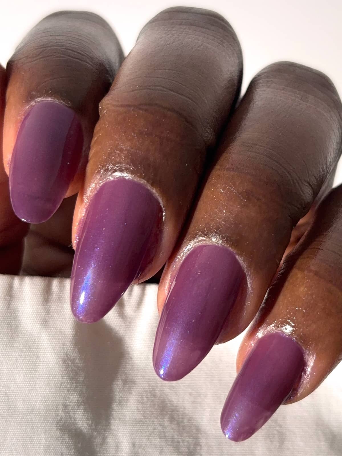 Eine Nahaufnahme einer Hand mit mandelförmigen Nägeln, lackiert in dem schimmernden Violettton „Gitti Nr. 063“, der zarte blaue Schimmerakzente aufweist.