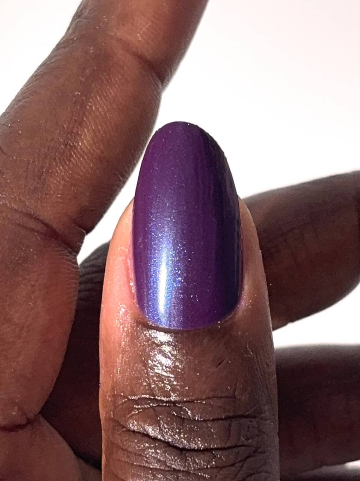 Eine Nahaufnahme einer Hand mit dunkler Haut zeigt einen Fingernagel, der mit glänzendem, schimmerndem lila Nagellack lackiert und mit dem „Silky Glaze Top Coat“ versiegelt wurde, um einen umwerfenden Glanzeffekt zu erzielen.