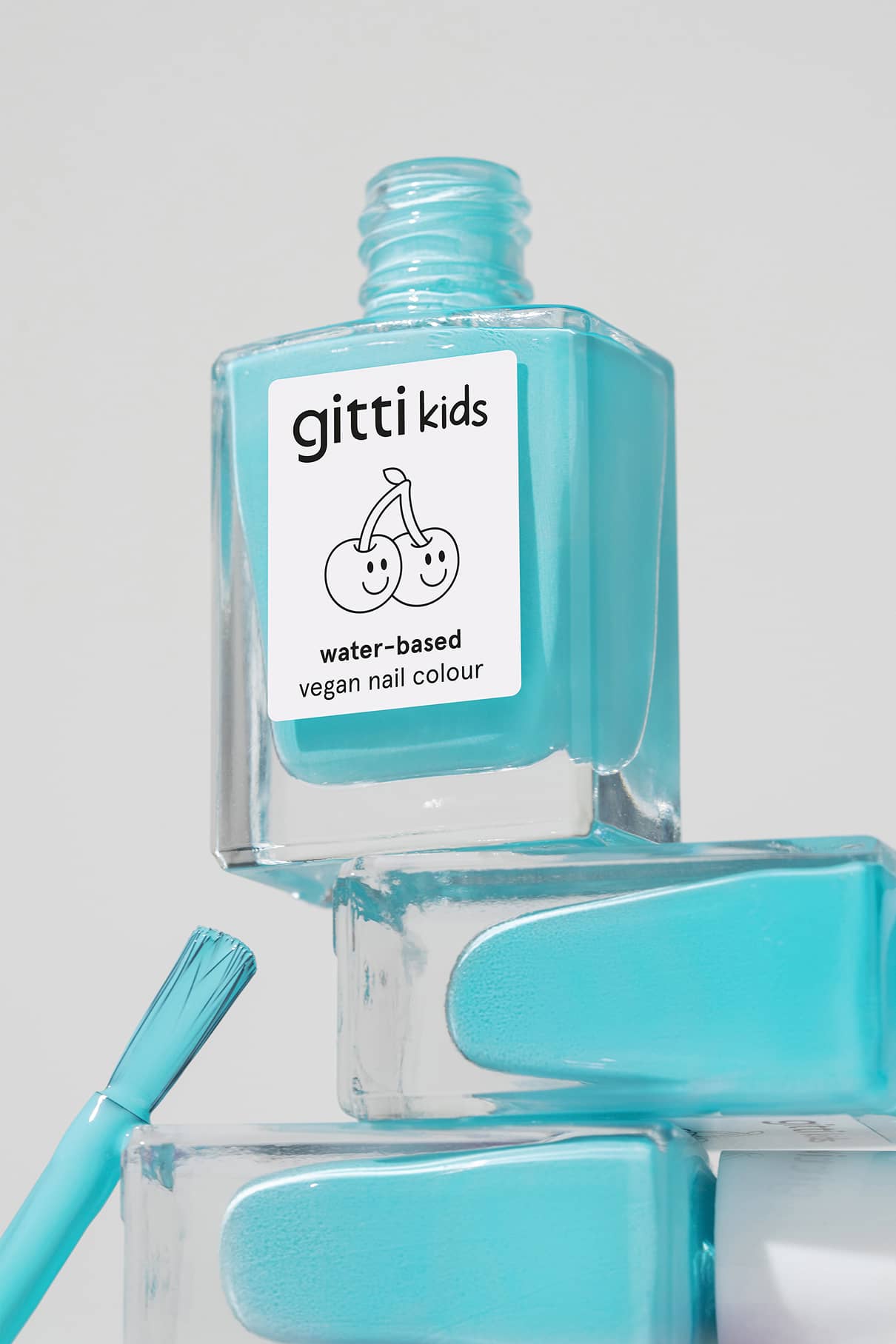 Eine Flasche gitti kids no. 01 türkis, kinderfreundliche Nagelfarbe mit einer Bürste und zwei gestapelten Flaschen darunter - ideal für Eltern, die sichere Kinderkosmetik suchen.