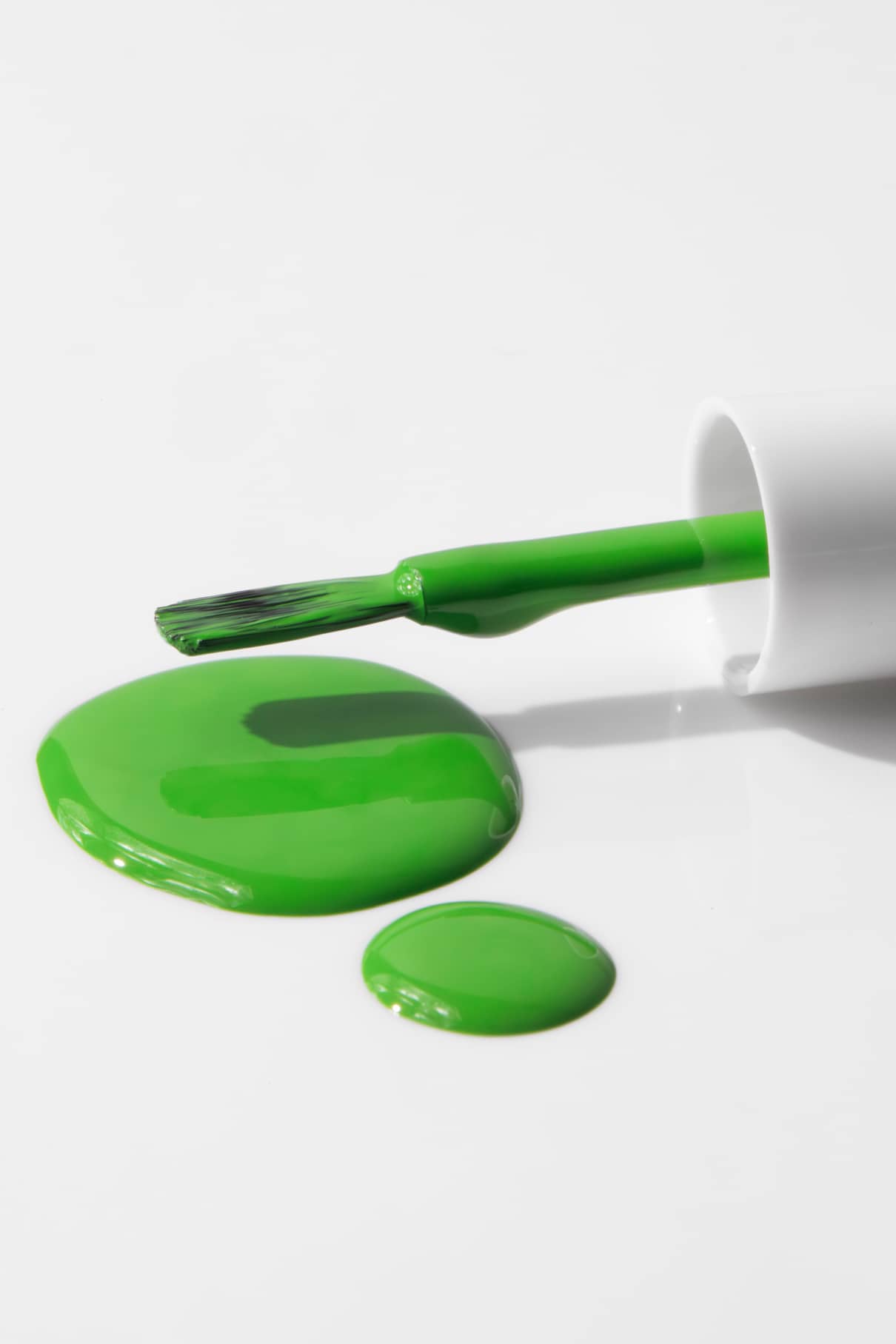 Ein Pinsel von gitti kids no. 04 grüner Nagellack liegt neben zwei Pfützen verschütteten grünen Lacks auf einer weißen Fläche.