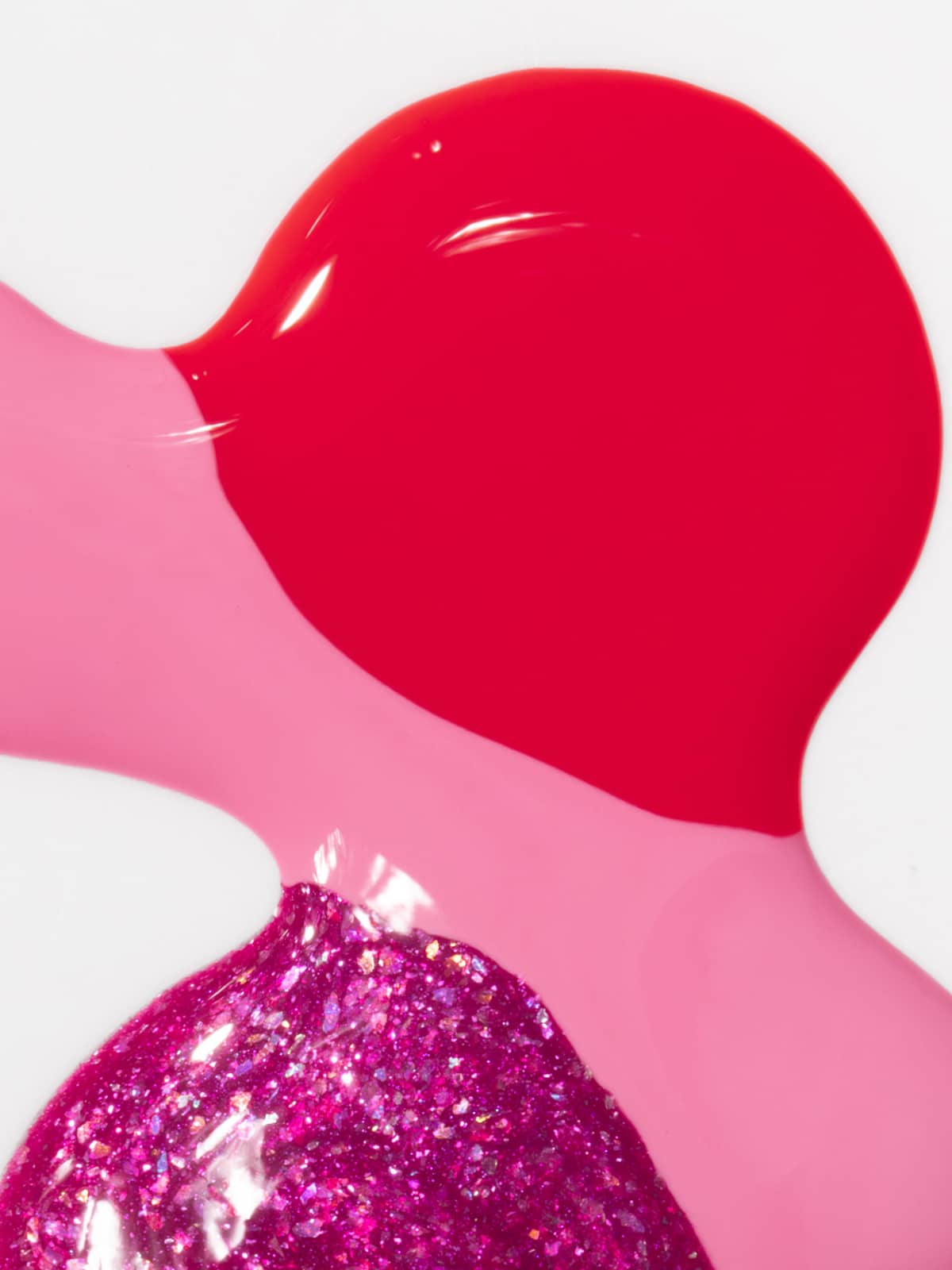 Rote, bubble-rosa und glitzernde magentafarbene Nagellackflecken überlagern sich auf einem weißen Untergrund und ergeben ein glänzendes, strukturiertes Erscheinungsbild, das an die verspielten Farbtöne des „Bright Moments“-Sets erinnert.