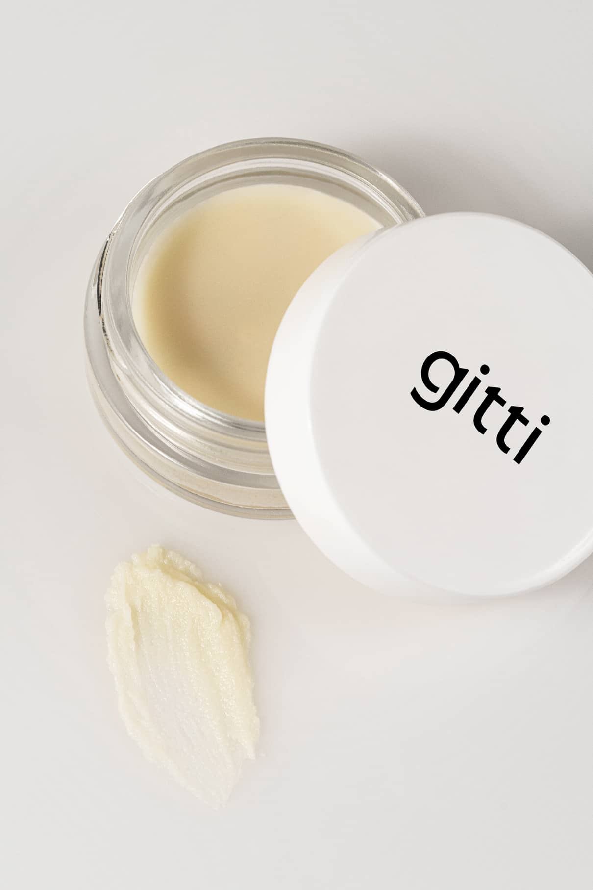 Ein kleines offenes Töpfchen mit einem weißen Deckel mit der Aufschrift gitti steht neben einem Klecks der Creme auf einer weißen Fläche - perfekt für die sanfte Entfernung der Pflanzenfarben von Plant Trio.