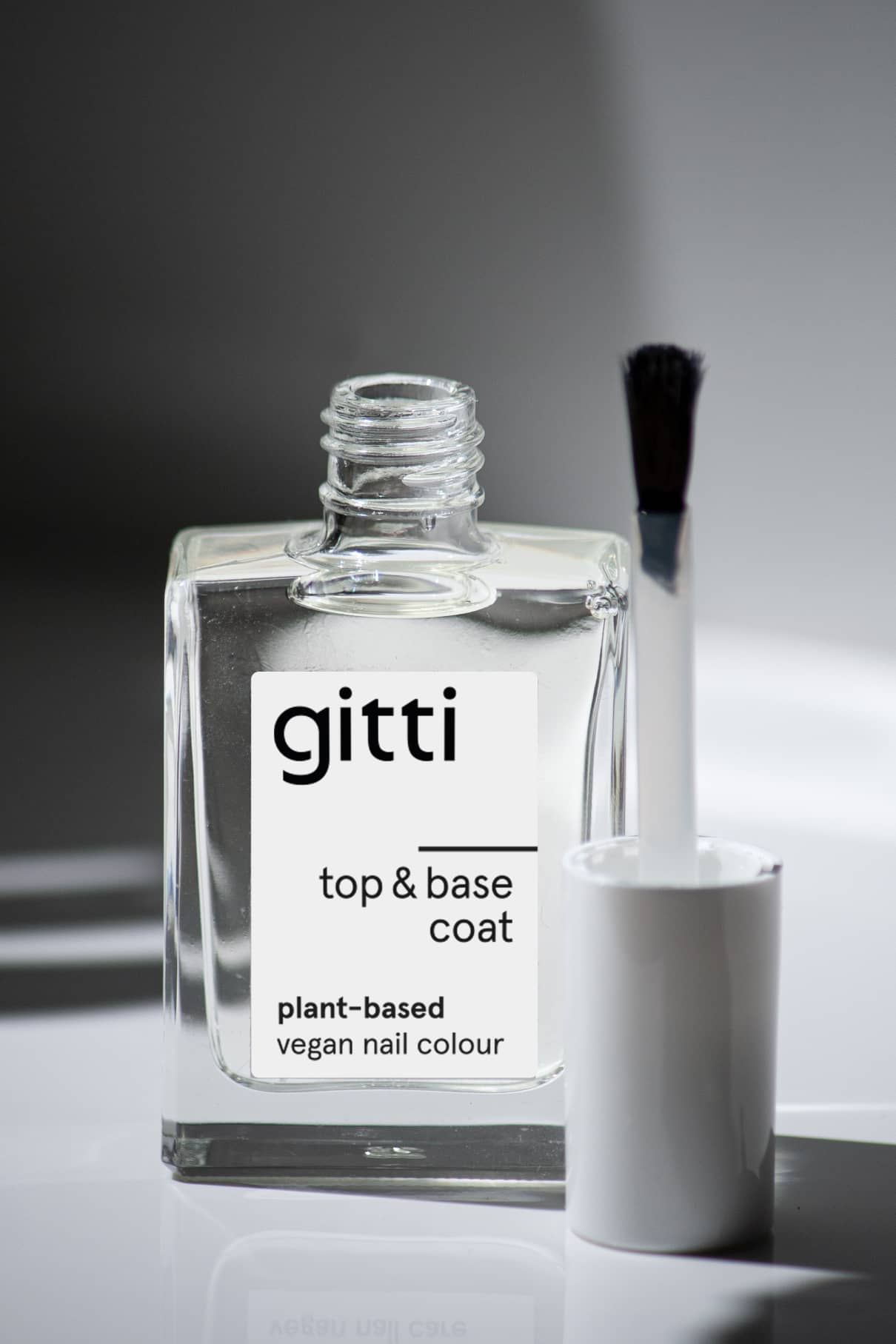 Eine offene Klarglasflasche mit der Aufschrift Plant-based Top&Base Coat und einem weißen Pinselapplikator daneben - Ihr 2-in-1-Produkt für zusätzlichen Halt und Glanz.