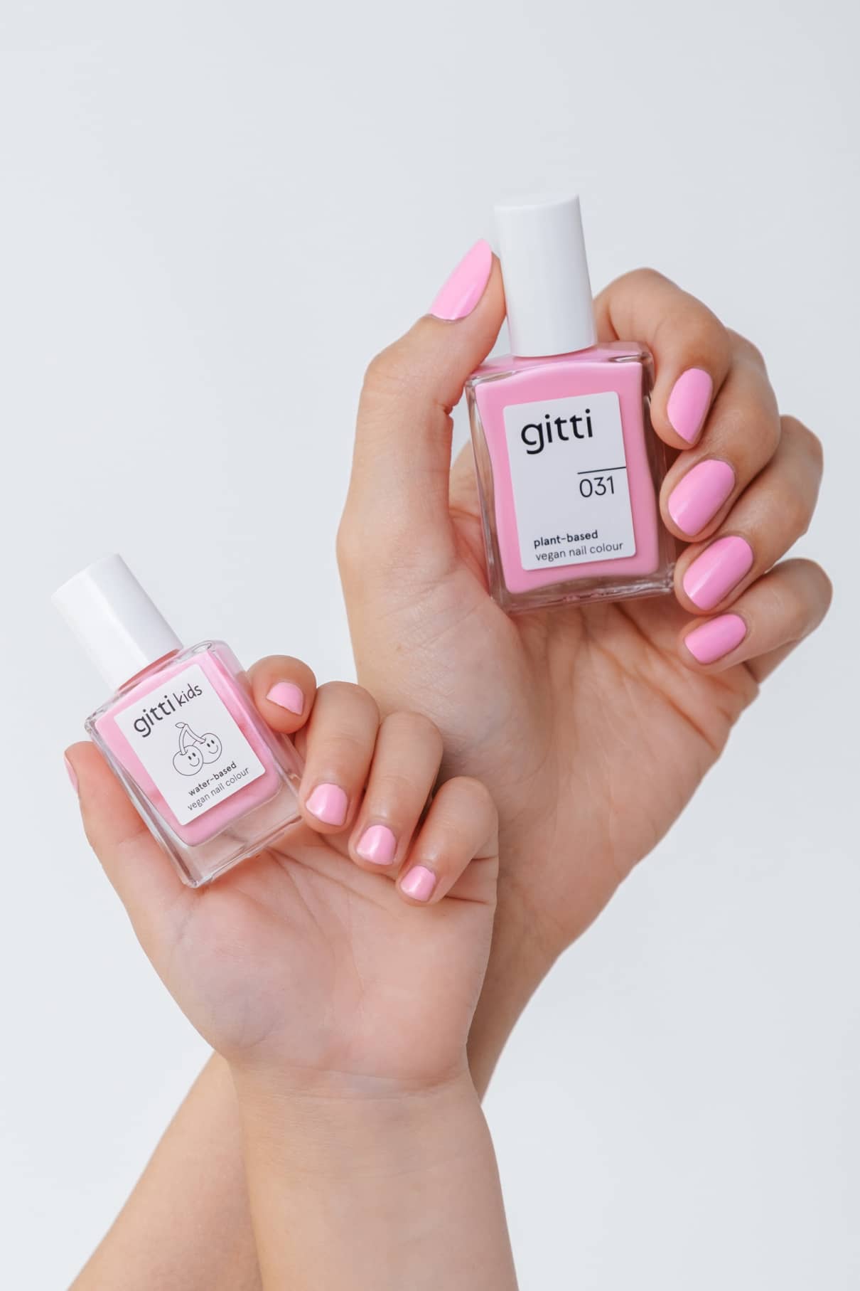 Zwei Hände mit rosa lackierten Nägeln halten Flaschen aus dem Mini & Me Set von Gitti, das veganen Nagellack auf pflanzlicher Basis in hellen Rosatönen vor einem schlichten weißen Hintergrund enthält.