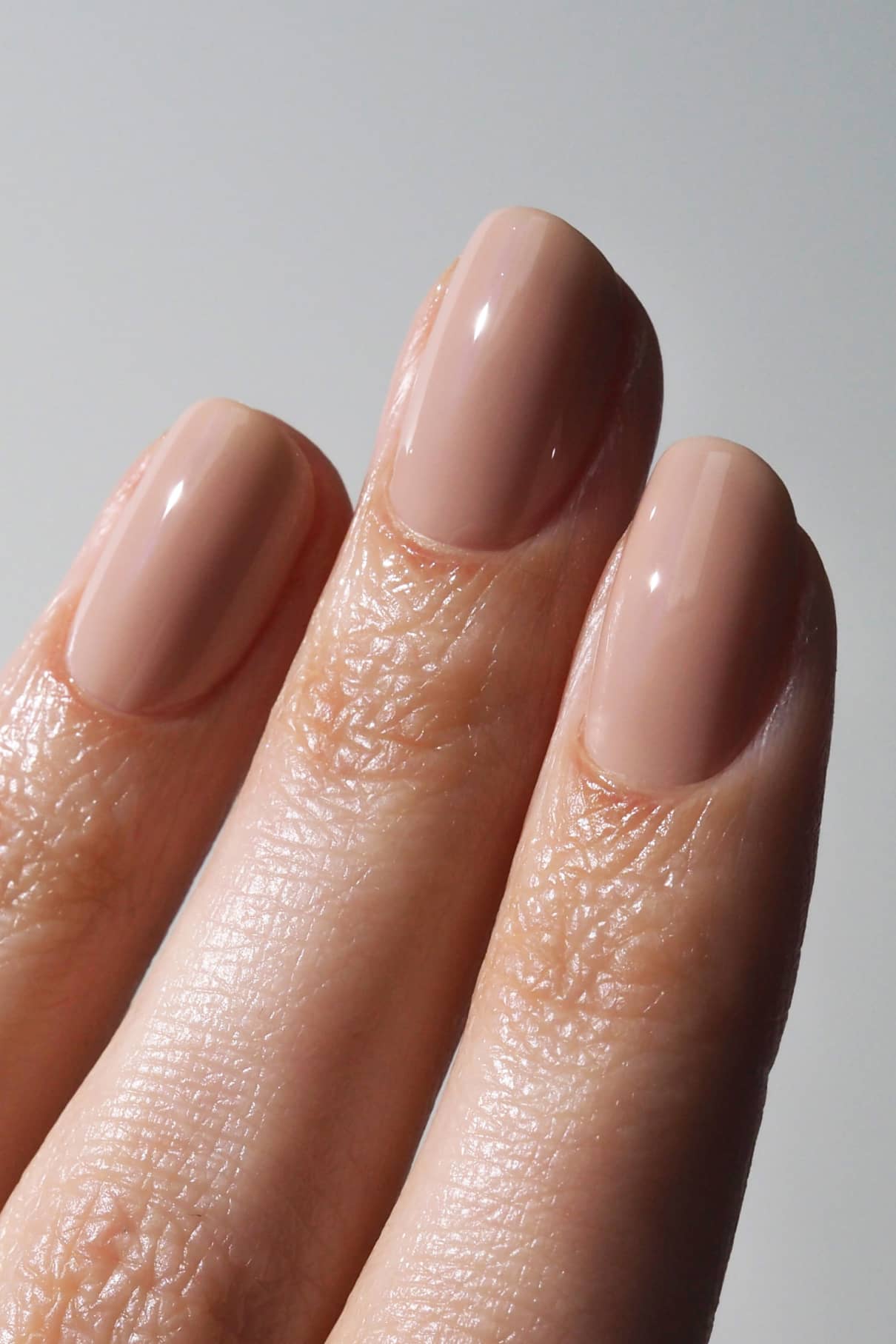 Nahaufnahme von drei Fingern mit kurzen, gepflegten Nägeln, lackiert in gitti no. 001, ein glänzender Beige-Ton für einen eleganten, natürlichen Look.