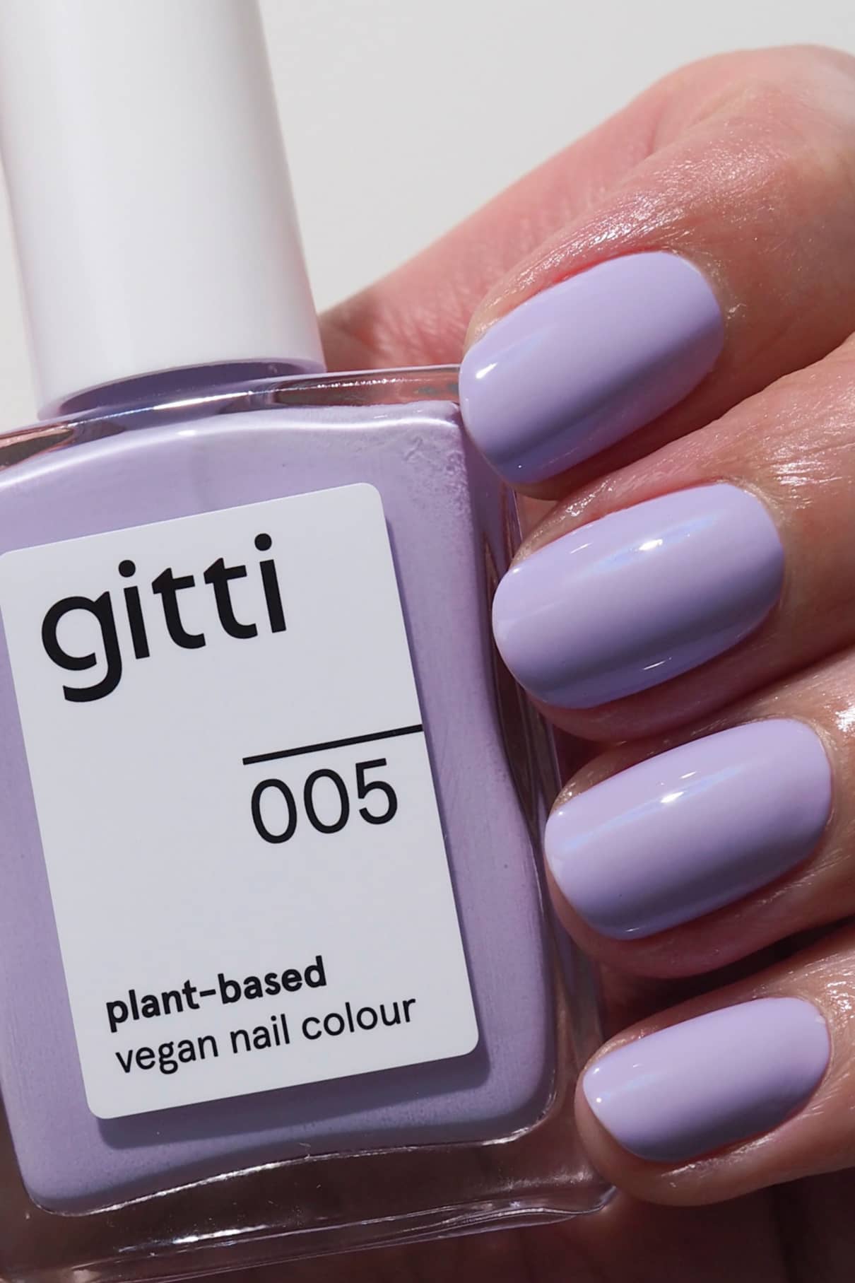 Eine Hand mit sauber manikürten, in einem harmonischen Lila-Ton lackierten Nägeln hält eine Flasche gitti no. 005, einem veganen Nagellack auf Pflanzenbasis.