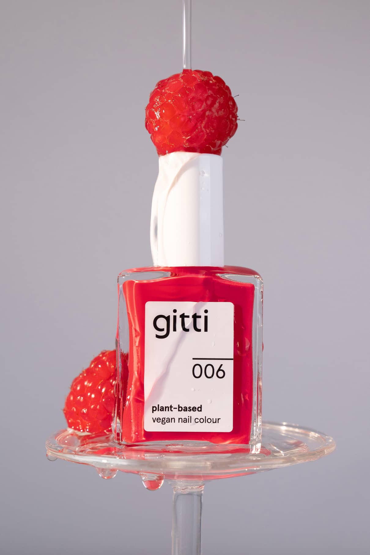 Eine Flasche gitti no. 006 pflanzliche, vegane Nagelfarbe, abgebildet mit einer Himbeere auf der Oberseite und flüssigen Tropfen, zeigt seinen leuchtenden Rotton mit rosa Unterton und eine verbesserte Formel für lang anhaltenden Glanz.