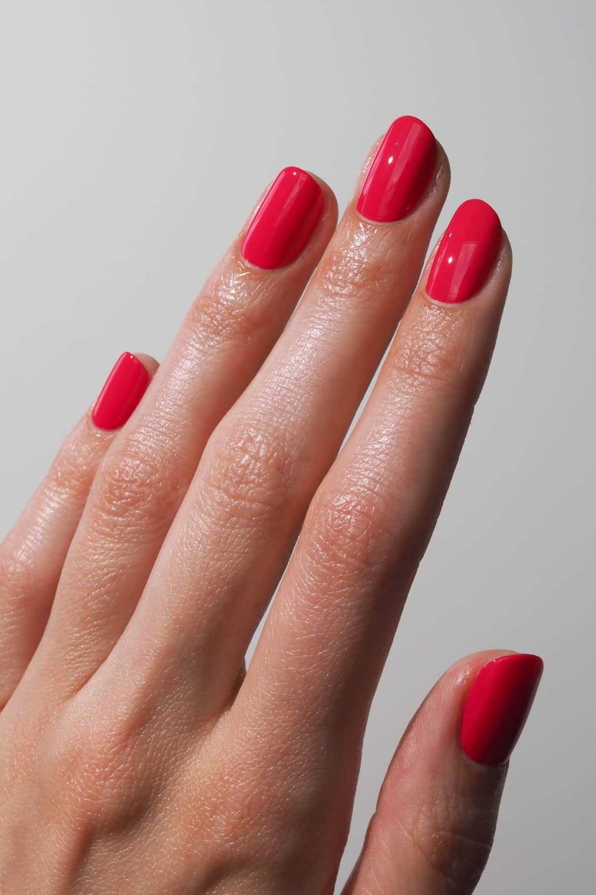Nahaufnahme einer Hand mit sauber manikürten Nägeln, die in gitti no. 006 - ein leuchtendes Rot mit glänzendem Finish und rosa Untertönen - vor einem unifarbenen Hintergrund.