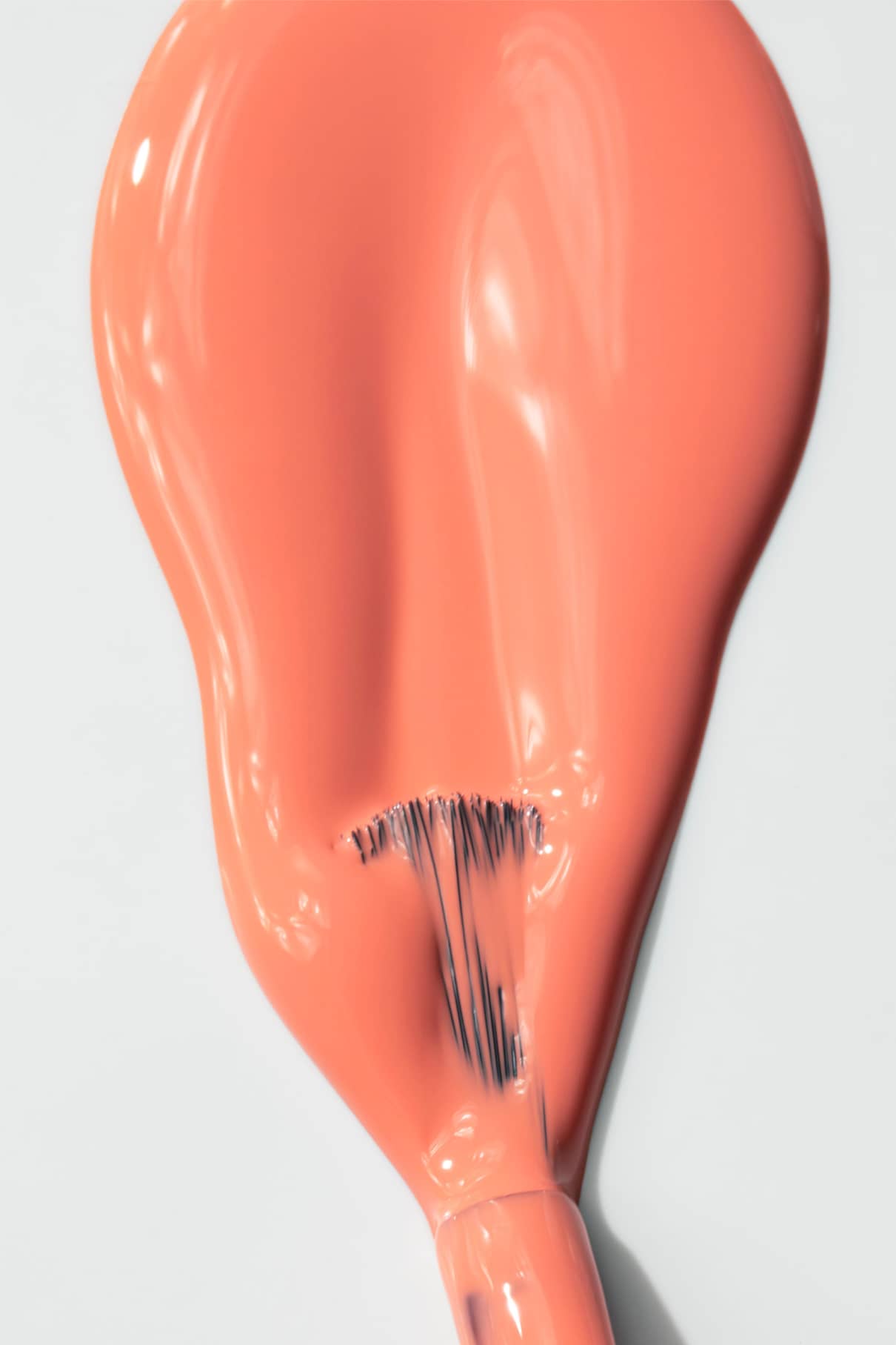 Nahaufnahme eines Pinsels, mit dem gitti no. 010 Nagellack in einem intensiven Korallenton auf. Er erzeugt einen glatten, glänzenden Strich auf einer weißen Oberfläche und hebt die elegante Farbnuance hervor.