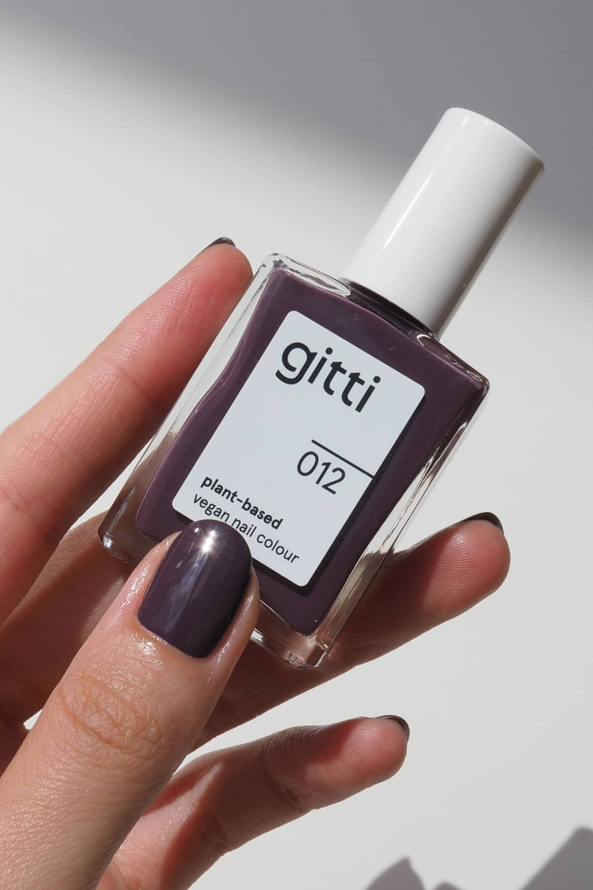 Close up of a hand holding gitti no. 012 vegan nail color bottle in a rich purple shade.