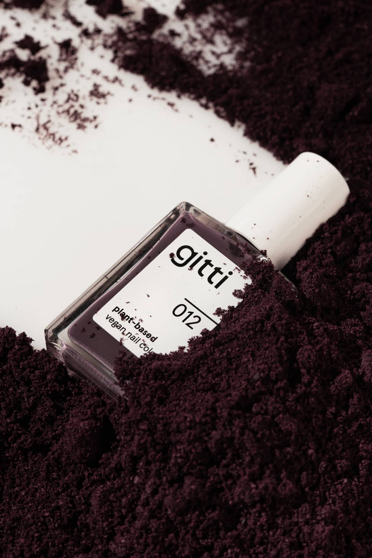 Gitti no. 012 vegan nail color bottle nestled in deep purple powder.