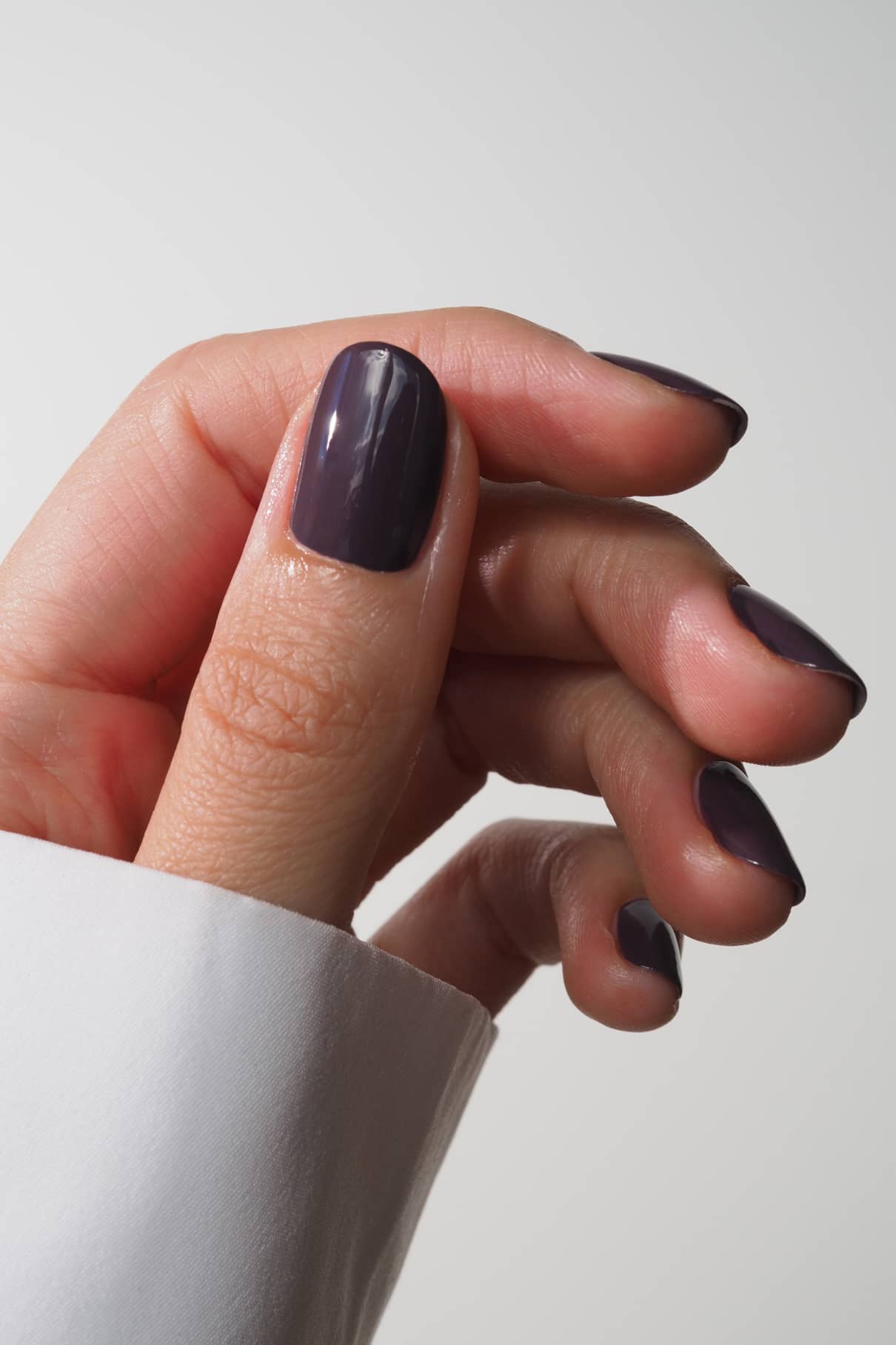 Close up of a glossy dark purple nail on a fingertip