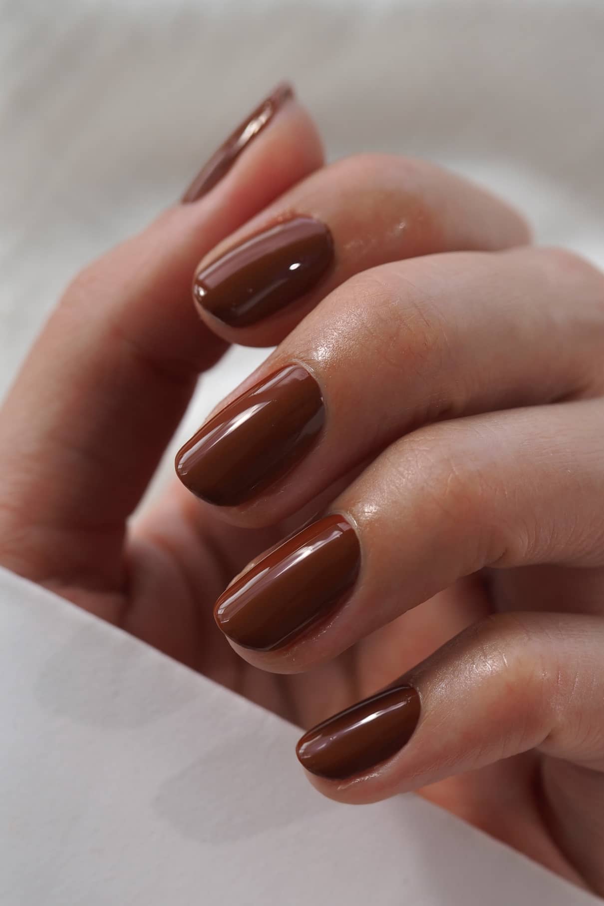 Eine Nahaufnahme einer Hand mit sauber manikürten Fingernägeln, die mit glänzendem Gitti Nr. 014, einem warmen braunen Nagellack, lackiert sind.