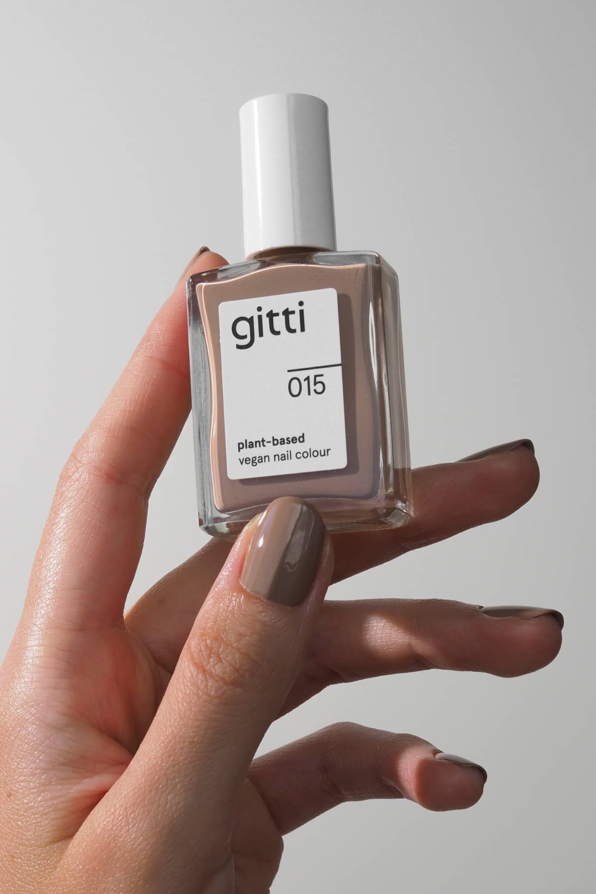 Eine Hand hält ein Fläschchen mit gitti no. 015; die Nägel sind in cremigem Beige lackiert, passend zum sanften Farbton der pflanzlichen veganen Nagelfarbe.