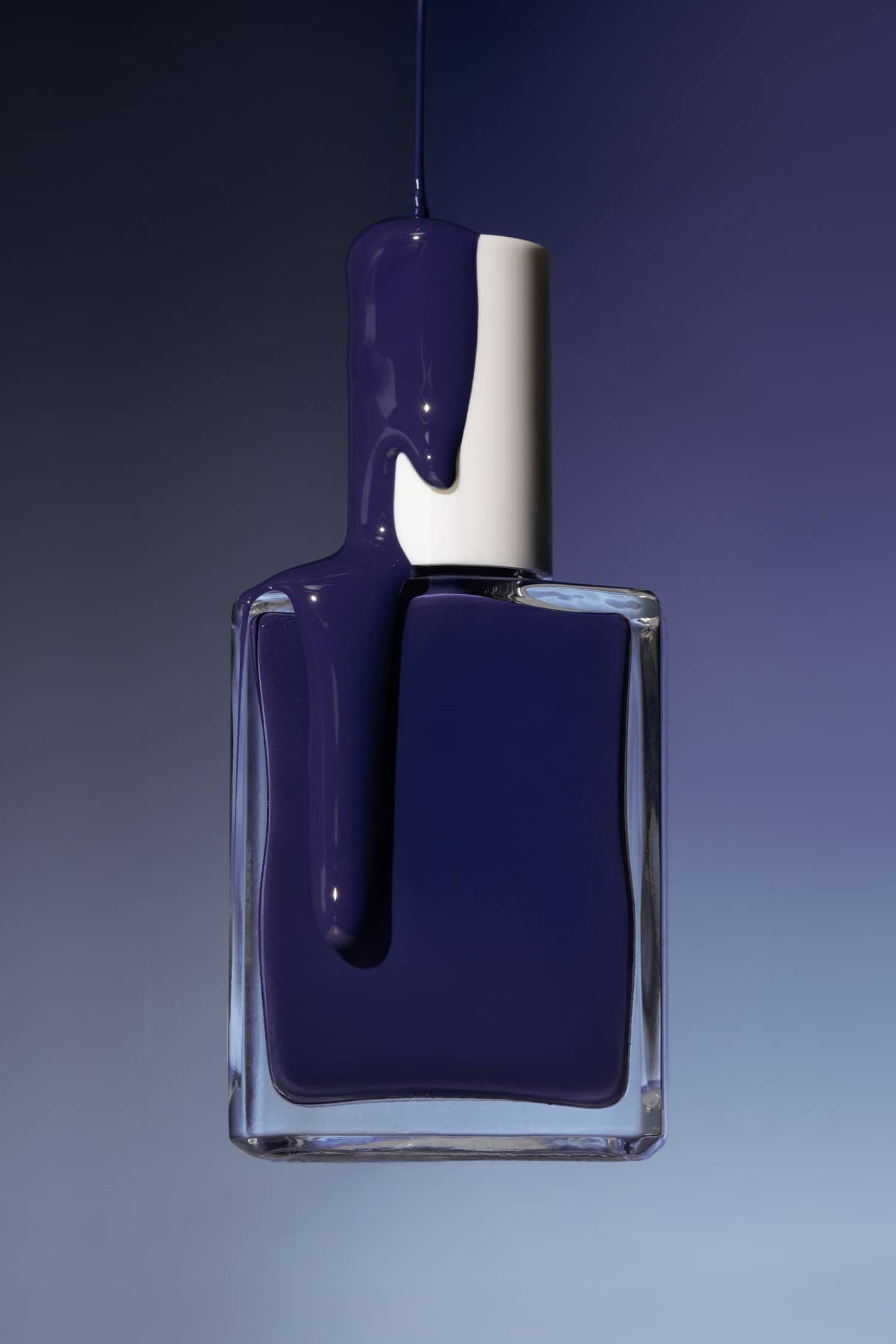 Eine Klarglasflasche mit silbernem Verschluss, teilweise gefüllt mit Gitti Nr. 018 - einer tiefblauen Politur - steht vor einem blauen Hintergrund mit Farbverlauf.