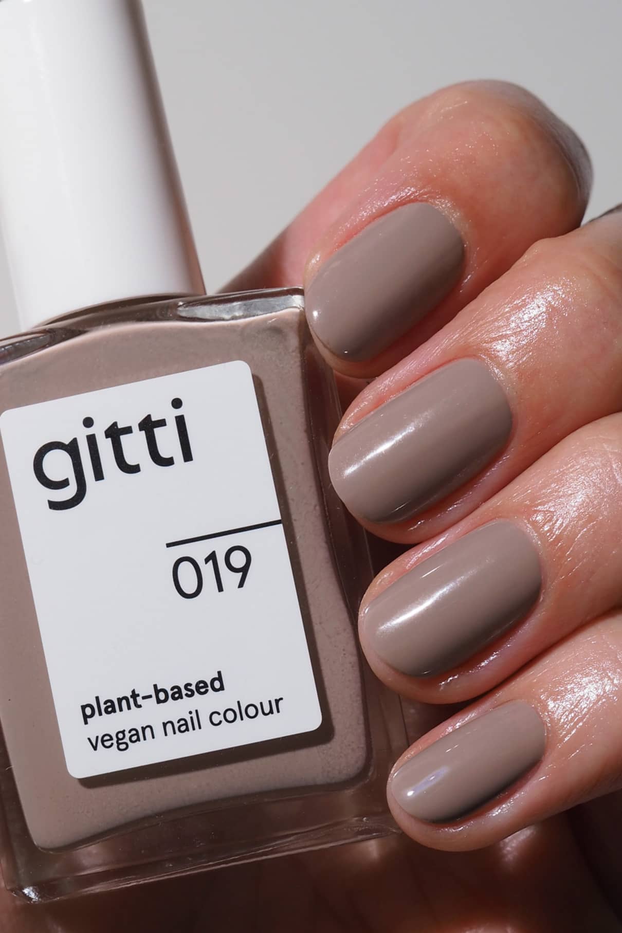 Eine Hand mit sauber manikürten, in zartem Mauve lackierten Nägeln, die eine Flasche gitti no. 019 pflanzlicher veganer Nagellack in einem passenden Farbton mit beigen Untertönen.