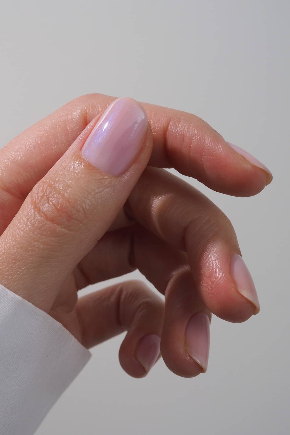 Nahaufnahme einer Hand mit glänzenden, halbtransparenten rosa Nägeln in gitti no. 025 vor einem schlichten, hellen Hintergrund.