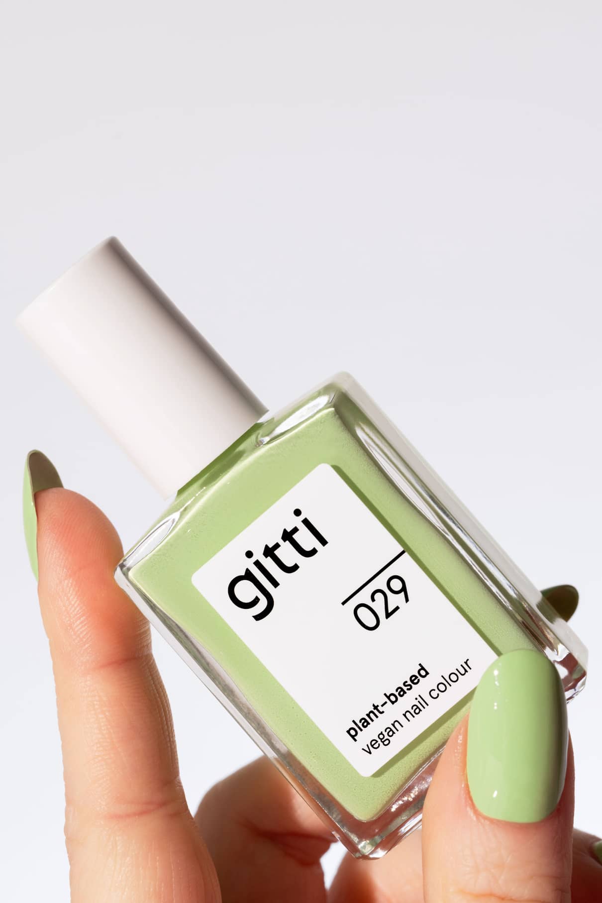 Eine Hand mit grün lackierten Nägeln hält eine Flasche von gitti no. 029, einer pflanzlichen, veganen Nagelfarbe in Pastellgrün - einem frischen, belebenden hellgrünen Farbton.