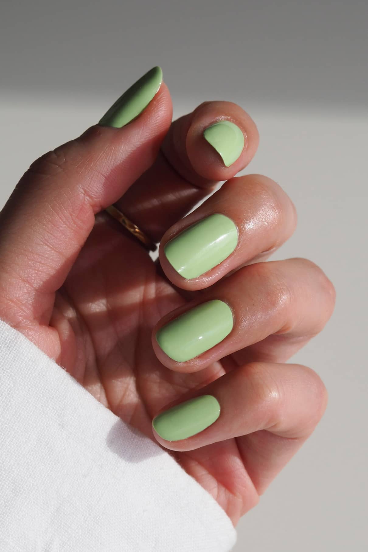 Eine Hand mit kurzen, sauber manikürten Nägeln, lackiert mit gitti no. 029, einem leuchtend grünen Nagellack, vor einem neutralen Hintergrund.