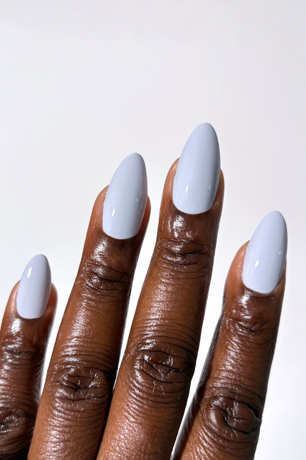 Eine Hand mit mitteldunklem Hautton zeigt mandelförmige Nägel, die mit glänzendem, kühlem blau-lavendelfarbenem gitti no. 050 lackiert sind, vor einem schlichten weißen Hintergrund.