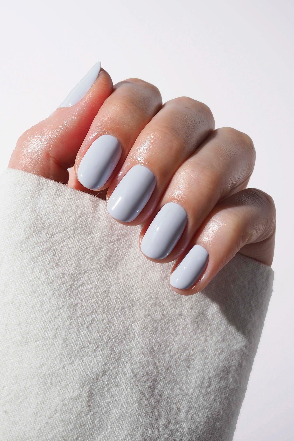 Eine Hand mit sauber manikürten Nägeln, lackiert in gitti no. 050, einem blassen Lavendelton mit einem Hauch von kühlem Blau, teilweise in weißes, strukturiertes Gewebe eingewickelt.