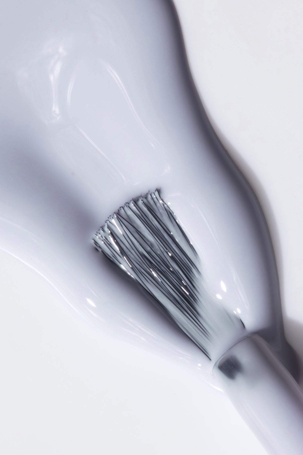 Nahaufnahme eines Pinsels, mit dem glänzender weißer gitti no. 050 Nagellack auf eine glatte Oberfläche auf, mit subtilen Reflexen in kühles Blau für einen frischen, modernen Look.