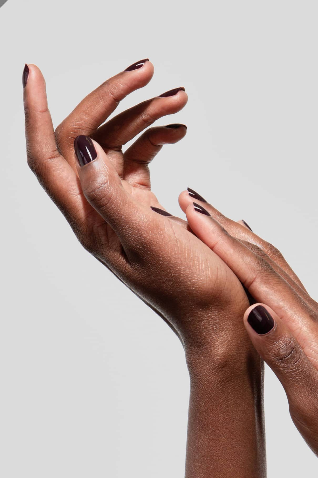 Zwei Hände mit gitti no. 103 Nagellack, einem tiefen Aubergine-Ton, sind anmutig vor einem schlichten hellgrauen Hintergrund posiert.