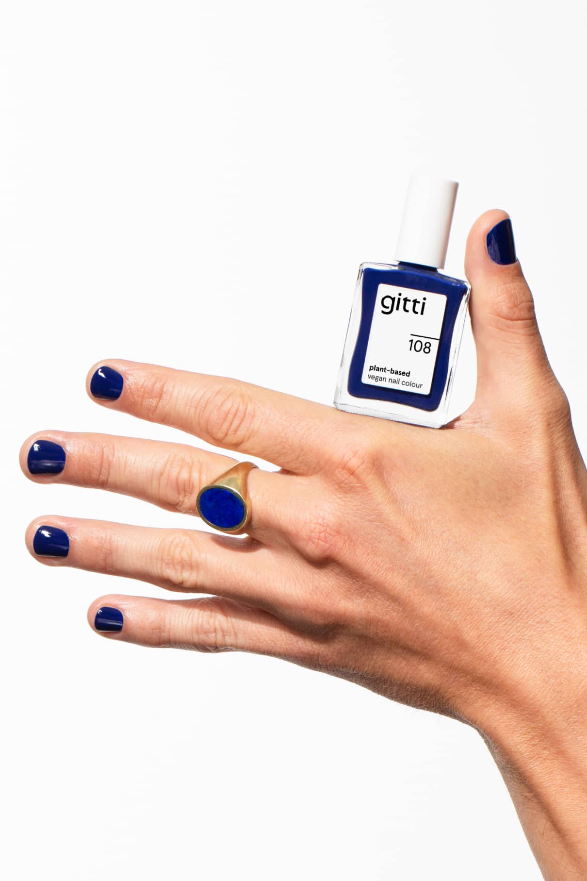 Eine Hand mit mitternachtsblauen Nägeln hält eine Flasche gitti no. 108; ein Goldring mit einem blauen Stein unterstreicht die leuchtend blaue Maniküre.