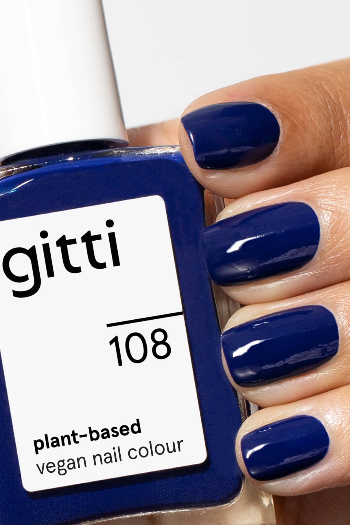 Eine Hand mit kurzen, intensiv blau lackierten Nägeln hält eine quadratische Flasche mit gitti no. 108, einem veganen Nagellack auf pflanzlicher Basis im gleichen nachtblauen Farbton.