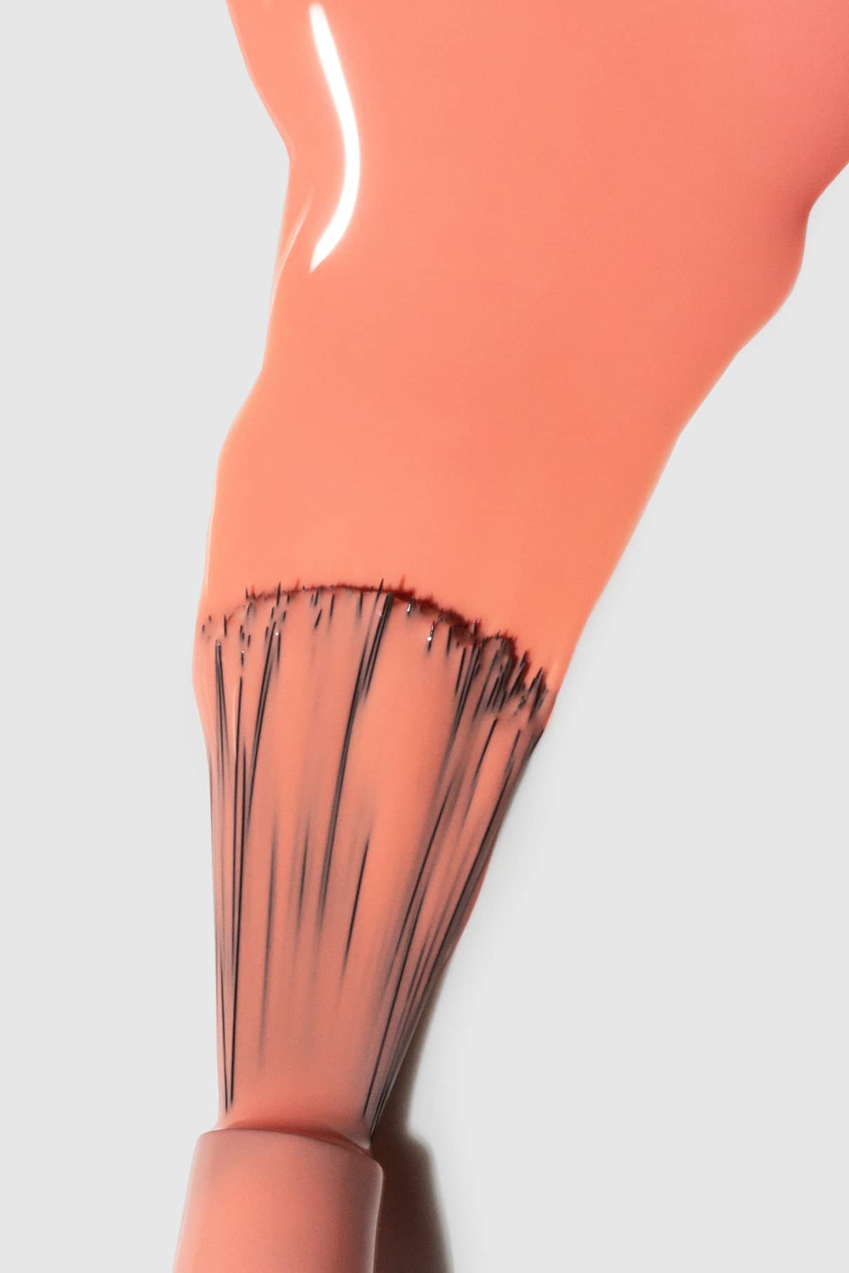 Nahaufnahme eines Nagellackpinsels mit gitti no. 111, ein zartes Pfirsichrosa mit warmen Untertönen, der auf eine weiße Fläche aufgetragen wird.