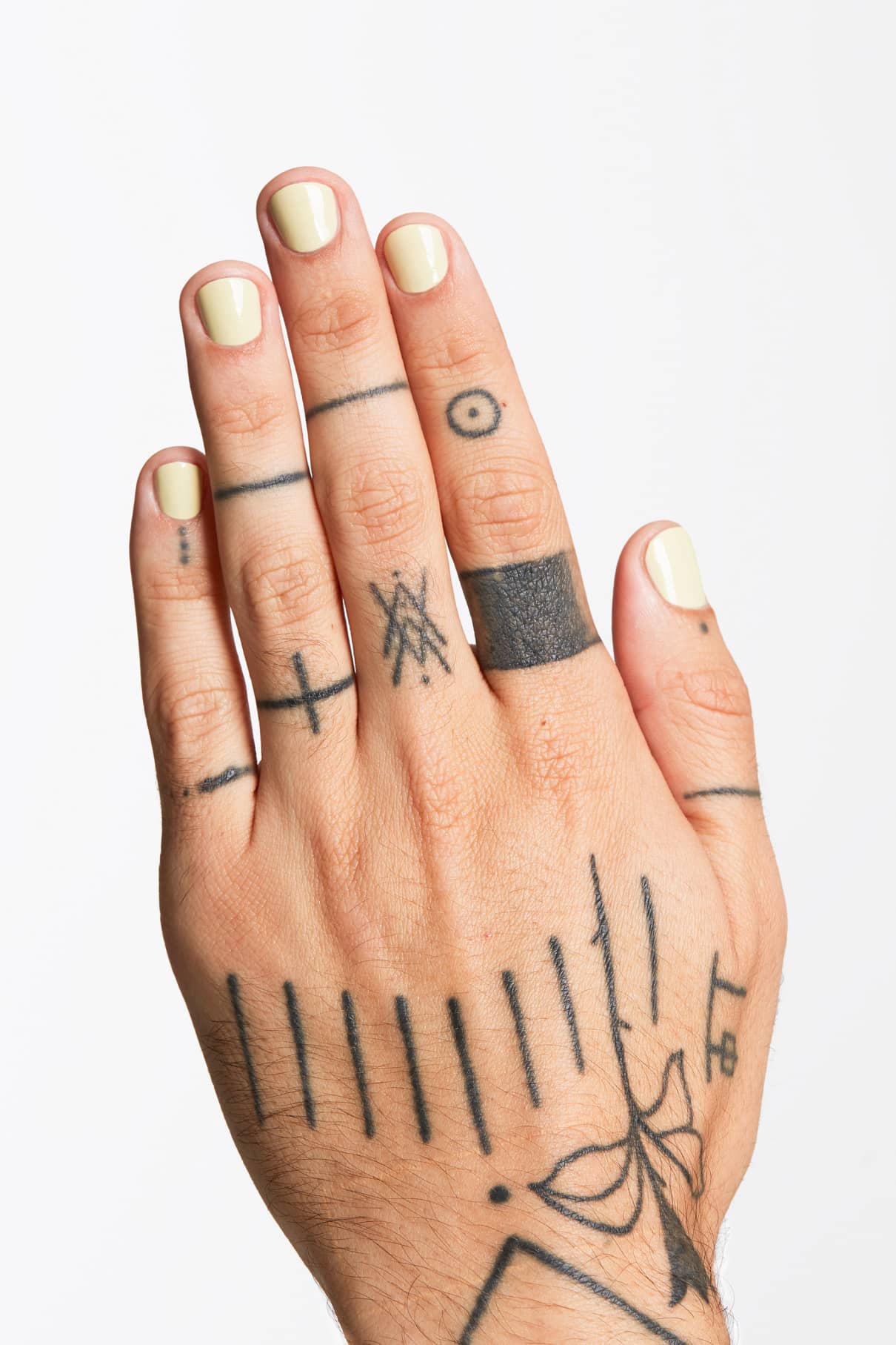 Eine Hand mit gitti no. 120 Pastellgrüner Nagellack und mehrere minimalistische schwarze Linien- und geometrische Tattoos auf den Fingern und dem Handrücken vor einem weißen Hintergrund.