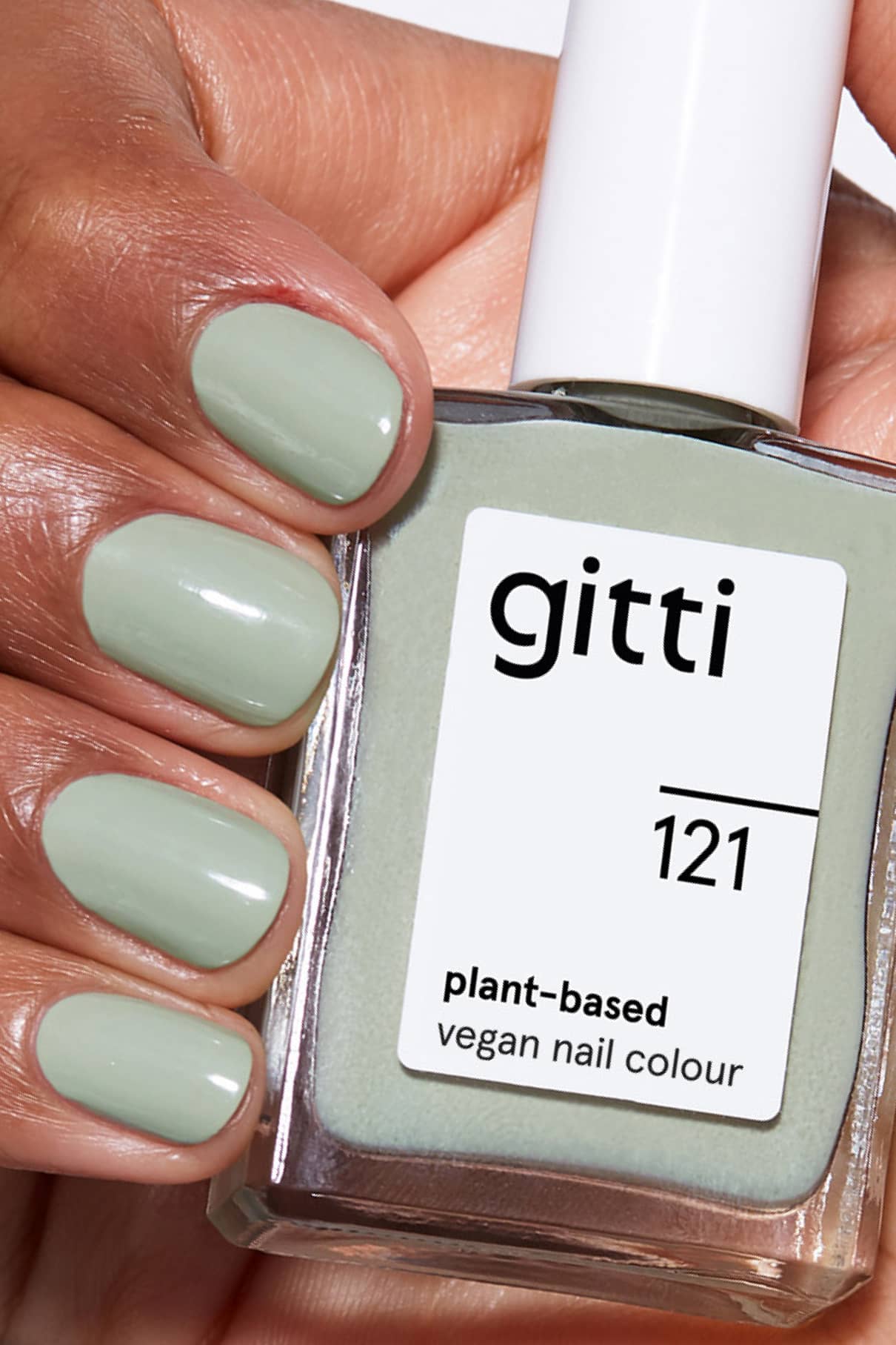 Eine Hand mit hellgrün lackierten Nägeln hält ein Fläschchen von gitti no. 121 - eine pflanzliche, vegane Nagelfarbe in Salbeigrün, ideal für Fans von dezenten Grüntönen, die so schick sind wie Ihre Lieblingswandfarbe.