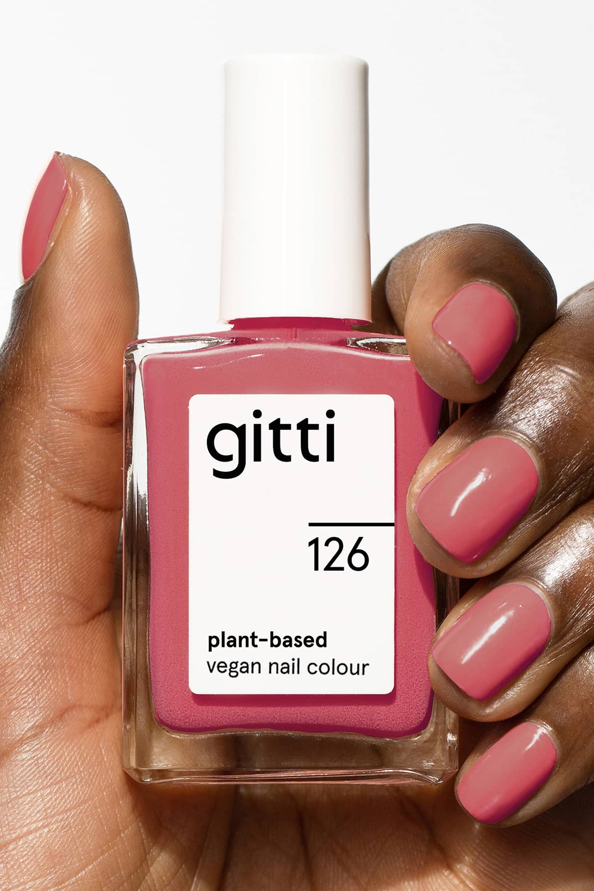 Eine Hand mit polierten Nägeln hält eine Flasche gitti no. 126, einer pflanzlichen, veganen Nagelfarbe in einem pastellfarbenen, sanft-roten Farbton.