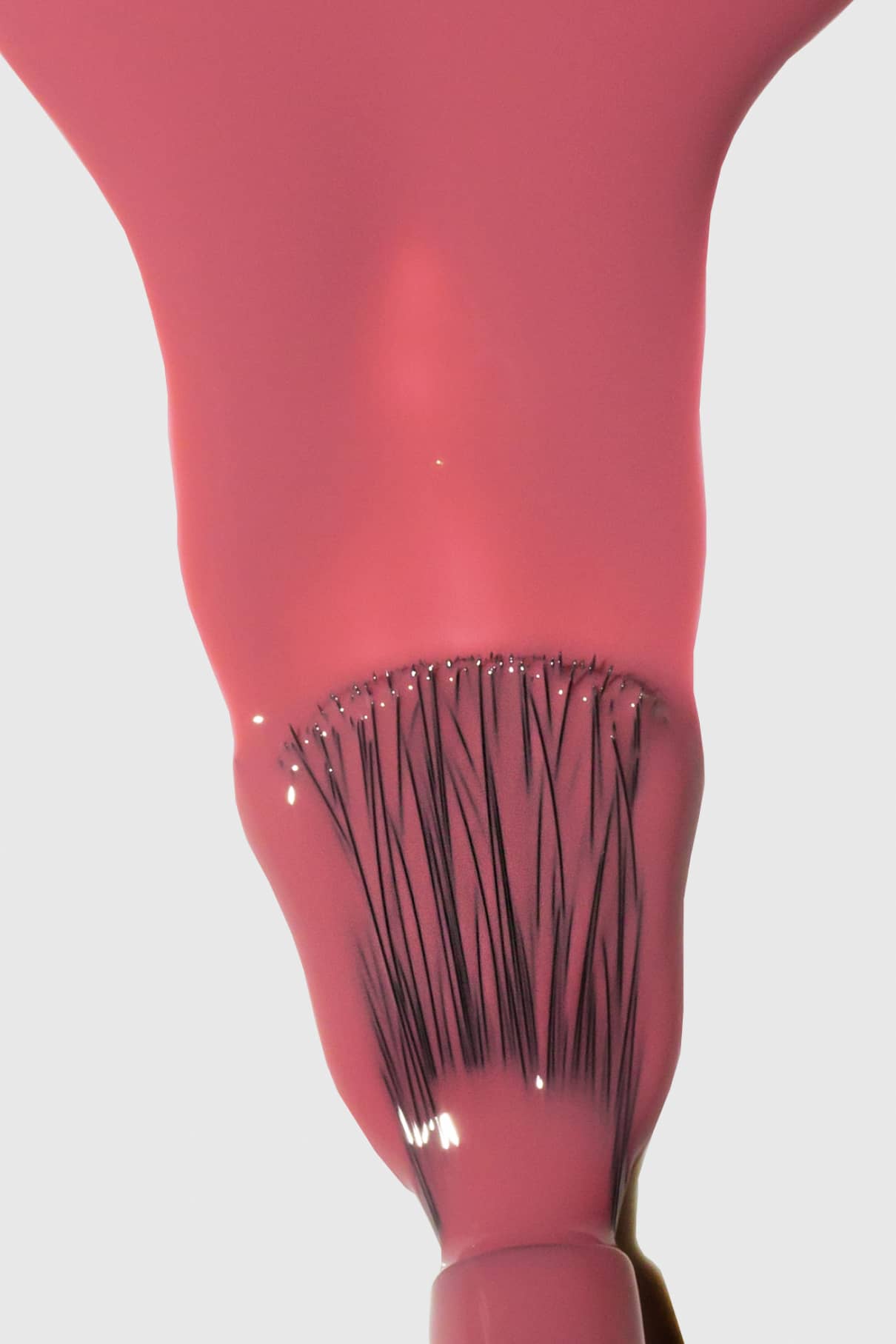 Nahaufnahme eines Pinsels, mit dem glänzender Gitti Nr. 126 Pastellrot-Nagellack, wobei die Borsten durch den nassen Lack auf weißem Hintergrund sichtbar sind.