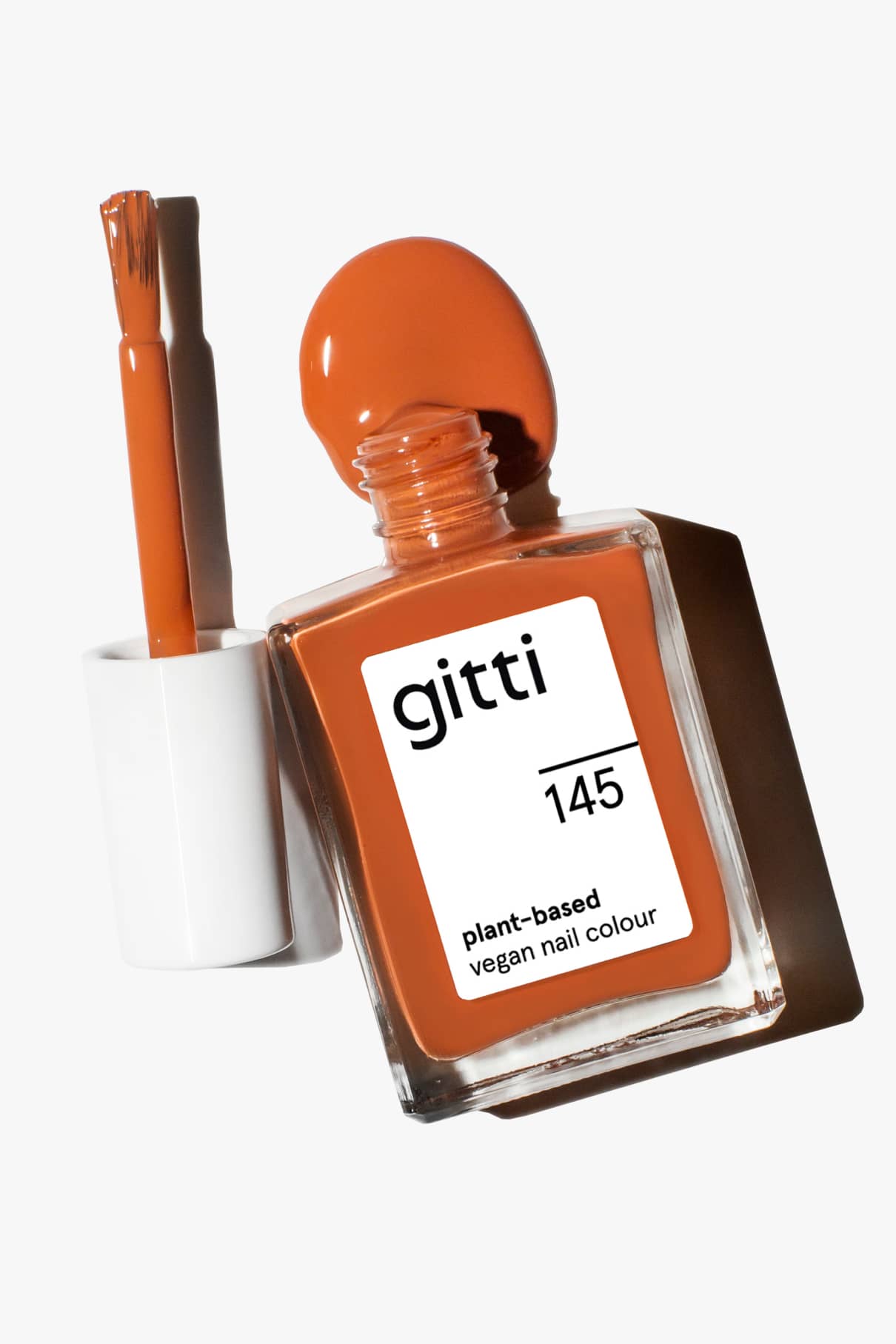 Eine Flasche orange-brauner veganer Nagellack, gitti no. 145 in Zimtbraun, mit dem Pinselapplikator daneben.