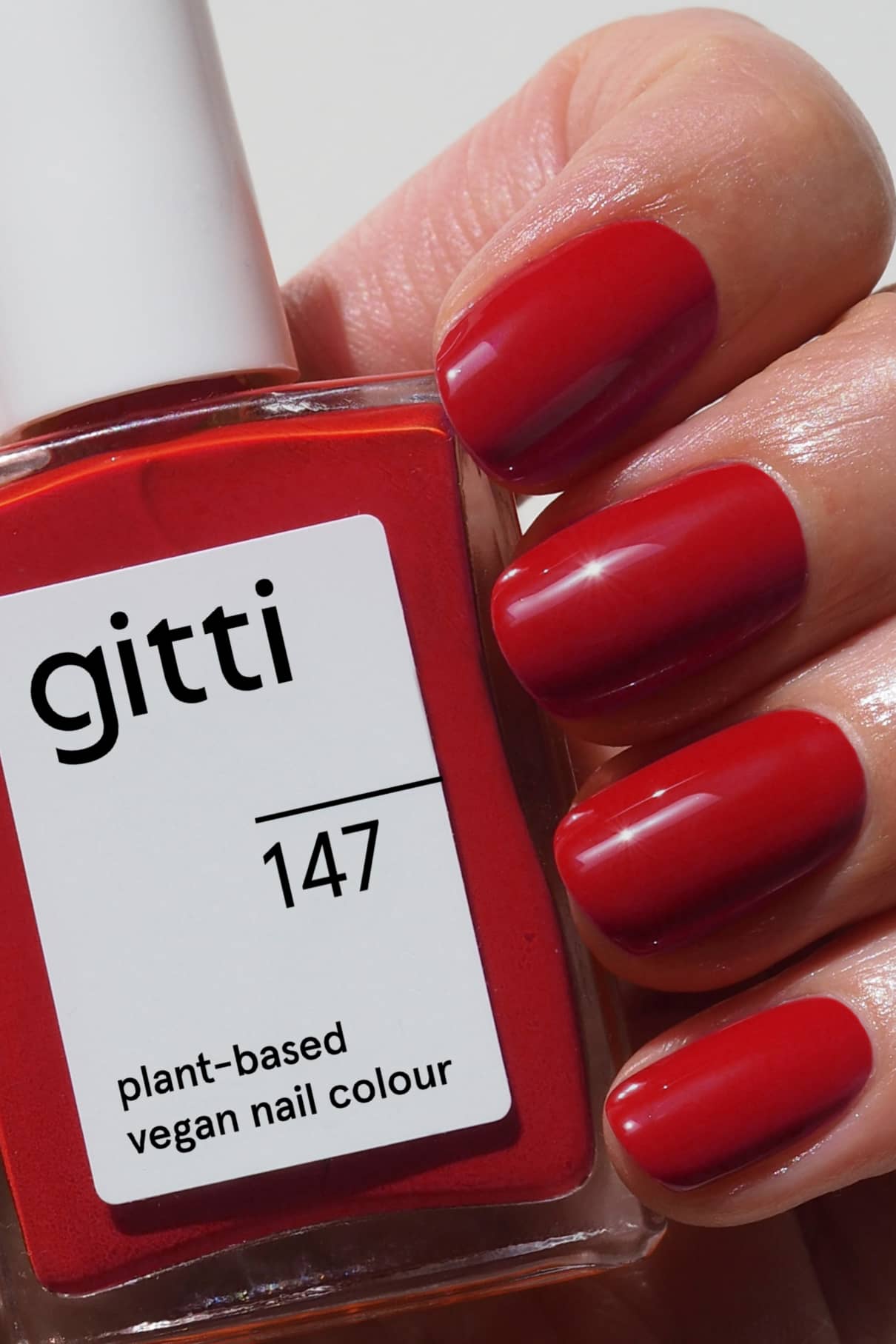 Eine Hand mit sauber manikürten roten Nägeln hält eine Flasche gitti no. 147 veganen Nagellack auf Pflanzenbasis in klassischem Rot.