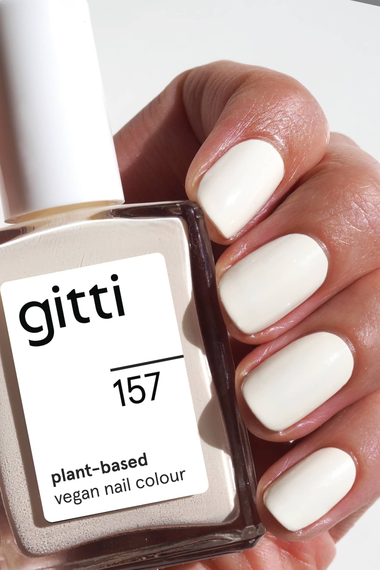 Eine Hand mit kurzen, sauber manikürten Nägeln, die in glänzendem Off-White-Lack lackiert sind, hält eine Flasche gitti no. 157 pflanzlicher veganer Nagellack.
