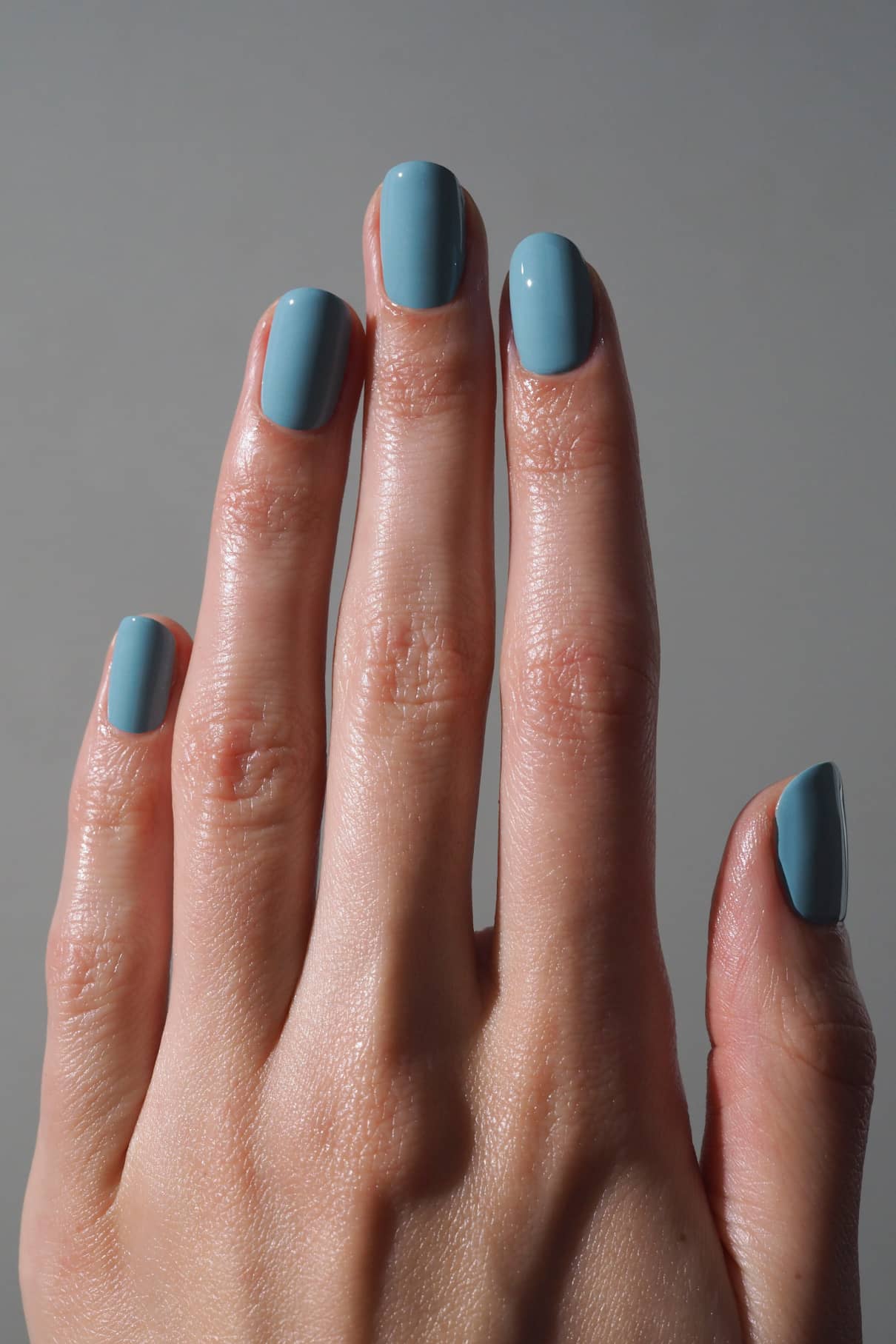 Eine Hand mit kurzen, sauber manikürten Nägeln, die im glänzend gedeckten Blauton der gitti no. 189, dargestellt vor einem schlichten grauen Hintergrund.