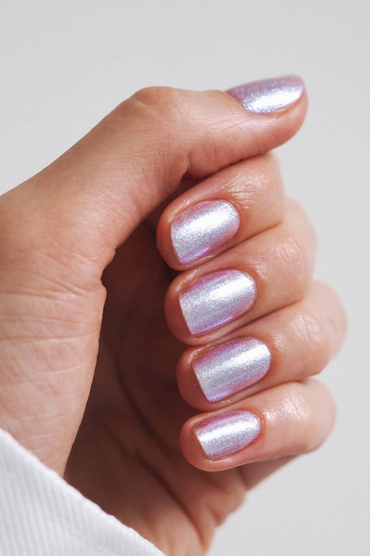 Eine Hand mit kurzen, sauber manikürten Nägeln, lackiert mit gitti no. 202, einem schimmernden, mehrfarbigen lavendelfarbenen Nagellack.