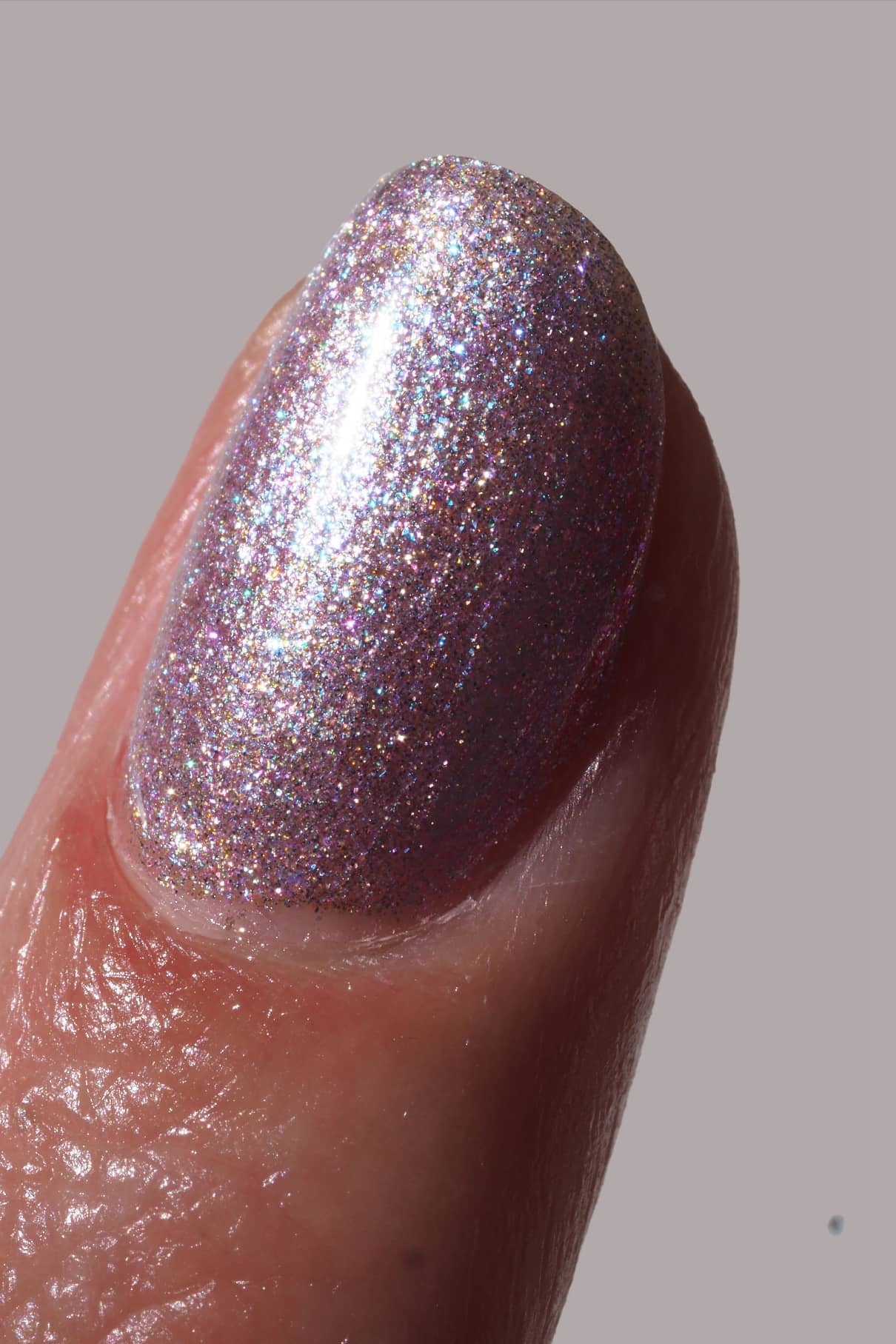 Nahaufnahme eines Fingernagels, der mit gitti no. 202, einem schimmernden, mehrfarbigen lavendelfarbenen Nagellack, vor einem einfarbigen Hintergrund.