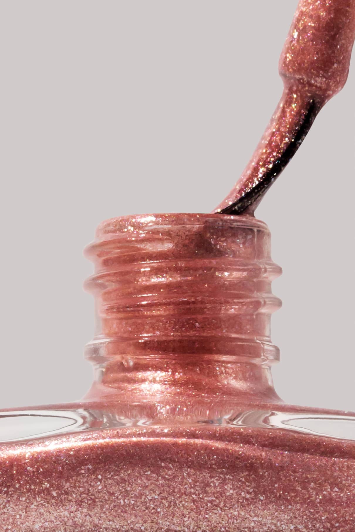 Nahaufnahme eines Pinsels, der in eine offene Flasche mit gitti no. 203, einem schimmernden, kupferfarbenen Nagellack, vor einem neutralen Hintergrund.