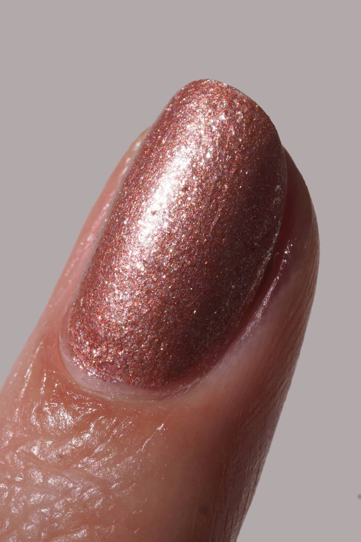 Nahaufnahme eines Fingers mit gitti no. 203, einem roséfarbenen, kupferfarbenen Glitzernagellack mit metallischem Finish, der auf den Fingernagel aufgetragen wurde.