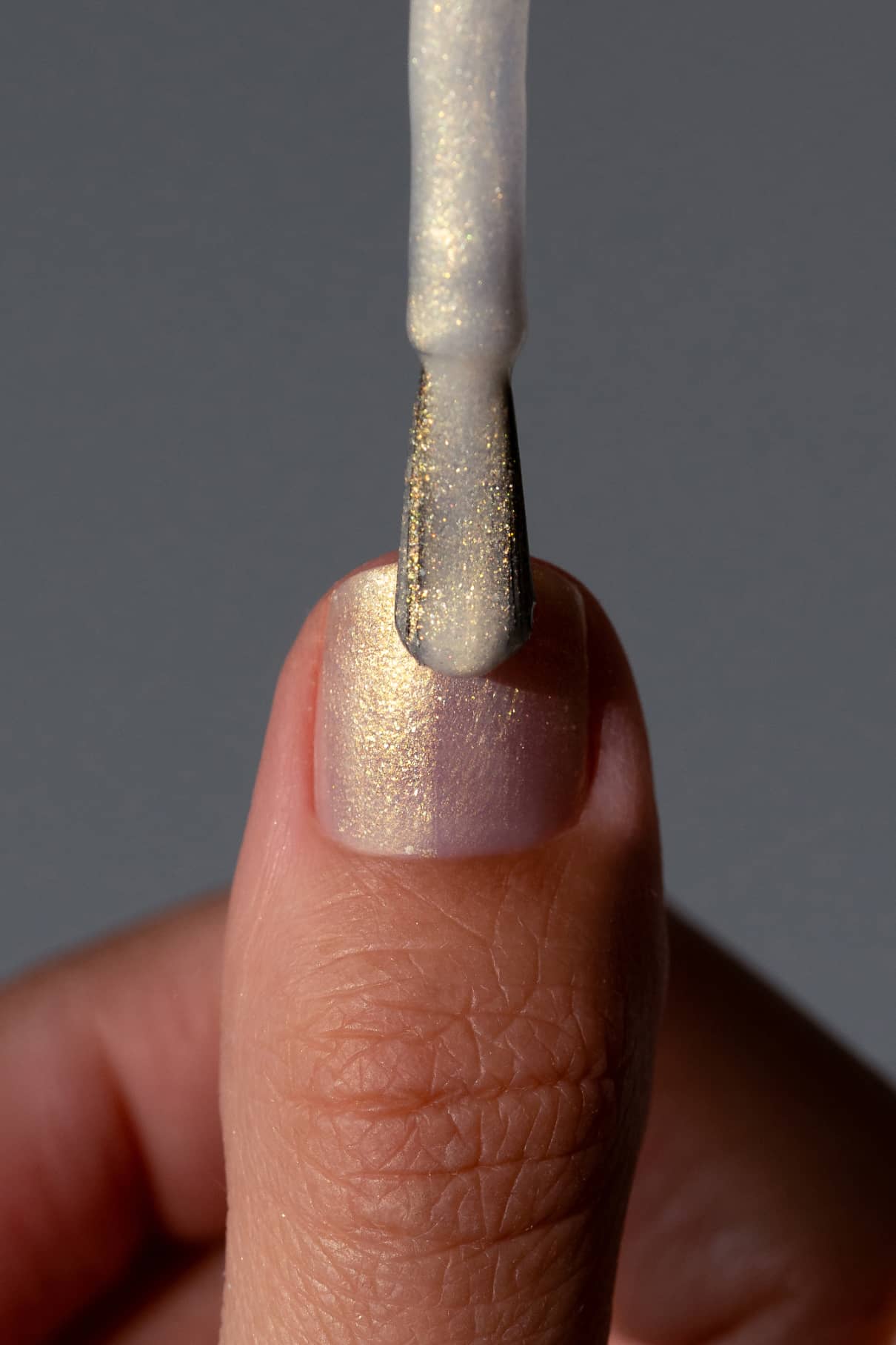 Eine Nahaufnahme eines Fingernagels, der mit gitti no. 207, einem schimmernden hellen Lack, mit einem Pinsel lackiert wird und ein eleganter irisierender Schimmer auf dem weißen Nagel entsteht.