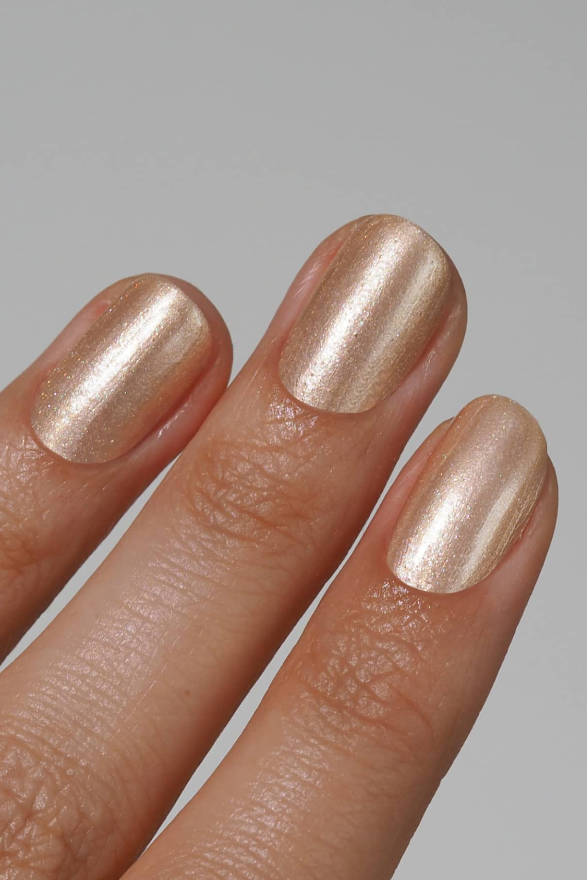 Eine Nahaufnahme von drei Fingern mit kurzen, sauber manikürten Nägeln, die mit gitti no. 208, einem schicken Metallic-Lack in Champagner oder hellem Gold.