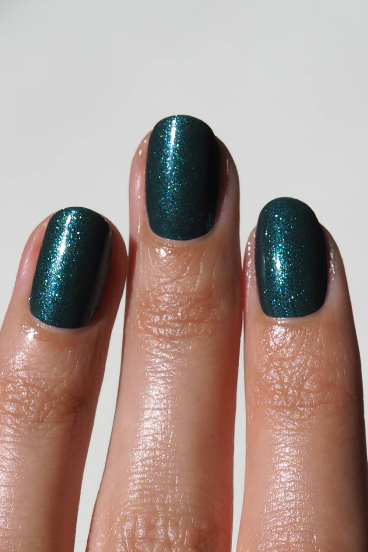 Nahaufnahme von drei Fingern mit sauber geschnittenen Nägeln, lackiert in gitti no. 211, einem schimmernden dunkelgrünen Farbton mit dezentem silber-blauem Schimmer.
