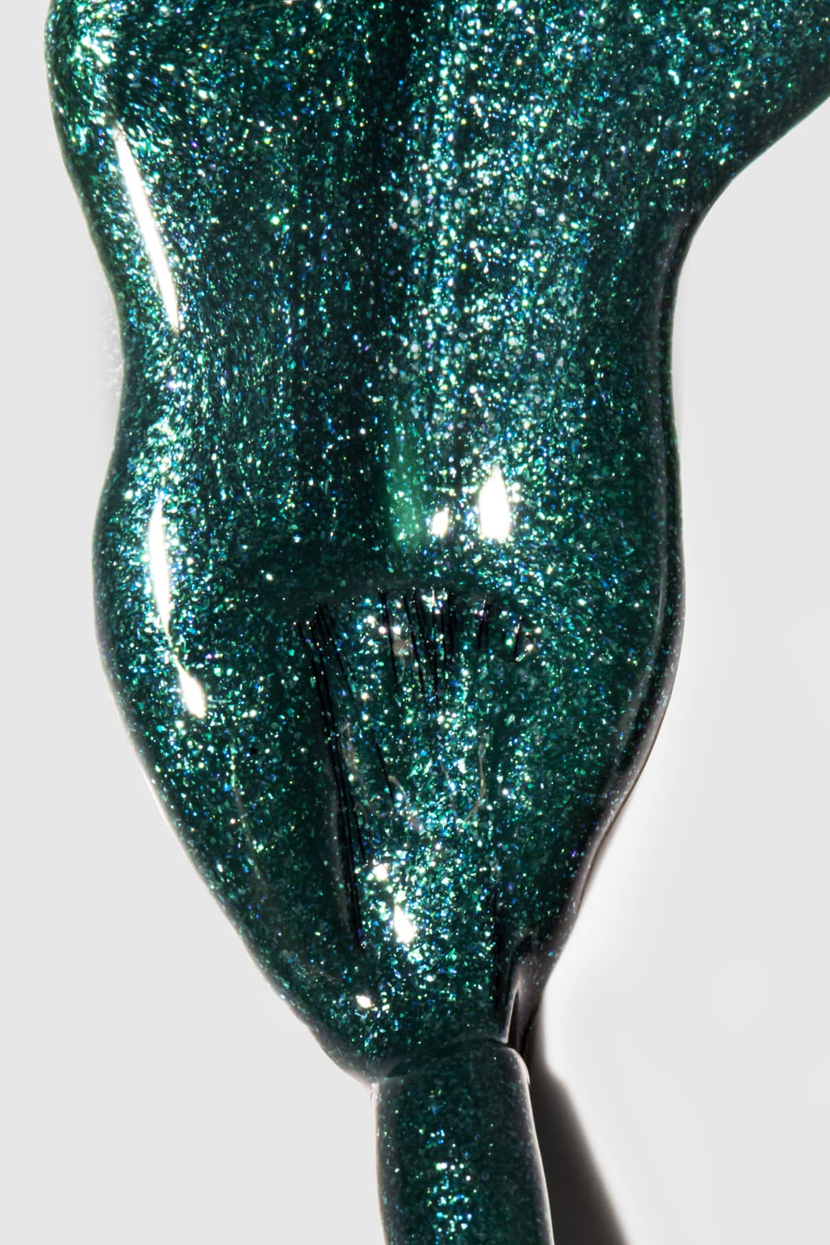 Nahaufnahme eines Pinsels, mit dem gitti no. 211, ein glitzernder dunkelgrüner Nagellack mit silberblauem Schimmer, auf eine weiße Fläche.
