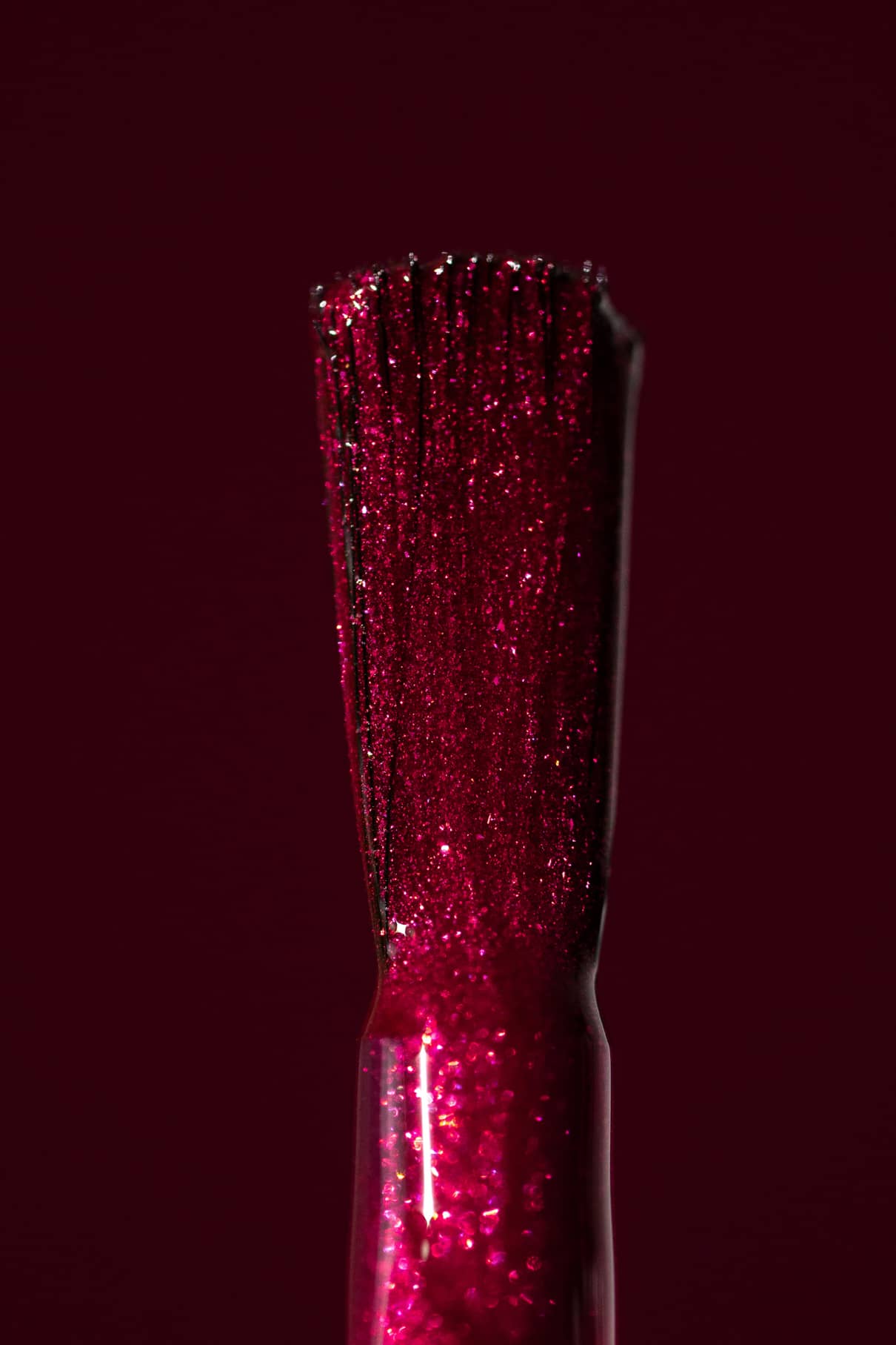 Nahaufnahme eines gitti no. 212 Pinsel mit rotem Glitzerlack vor einem passenden Hintergrund in tiefem bierigem Rot mit metallischem Schimmer.