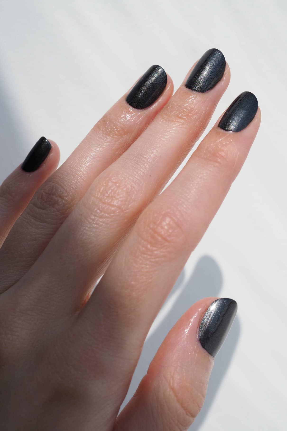 Eine Hand mit sauber manikürten Nägeln, lackiert mit gitti no. 303, einem schwarz-silbrigem Metallic-Finish Nagellack.