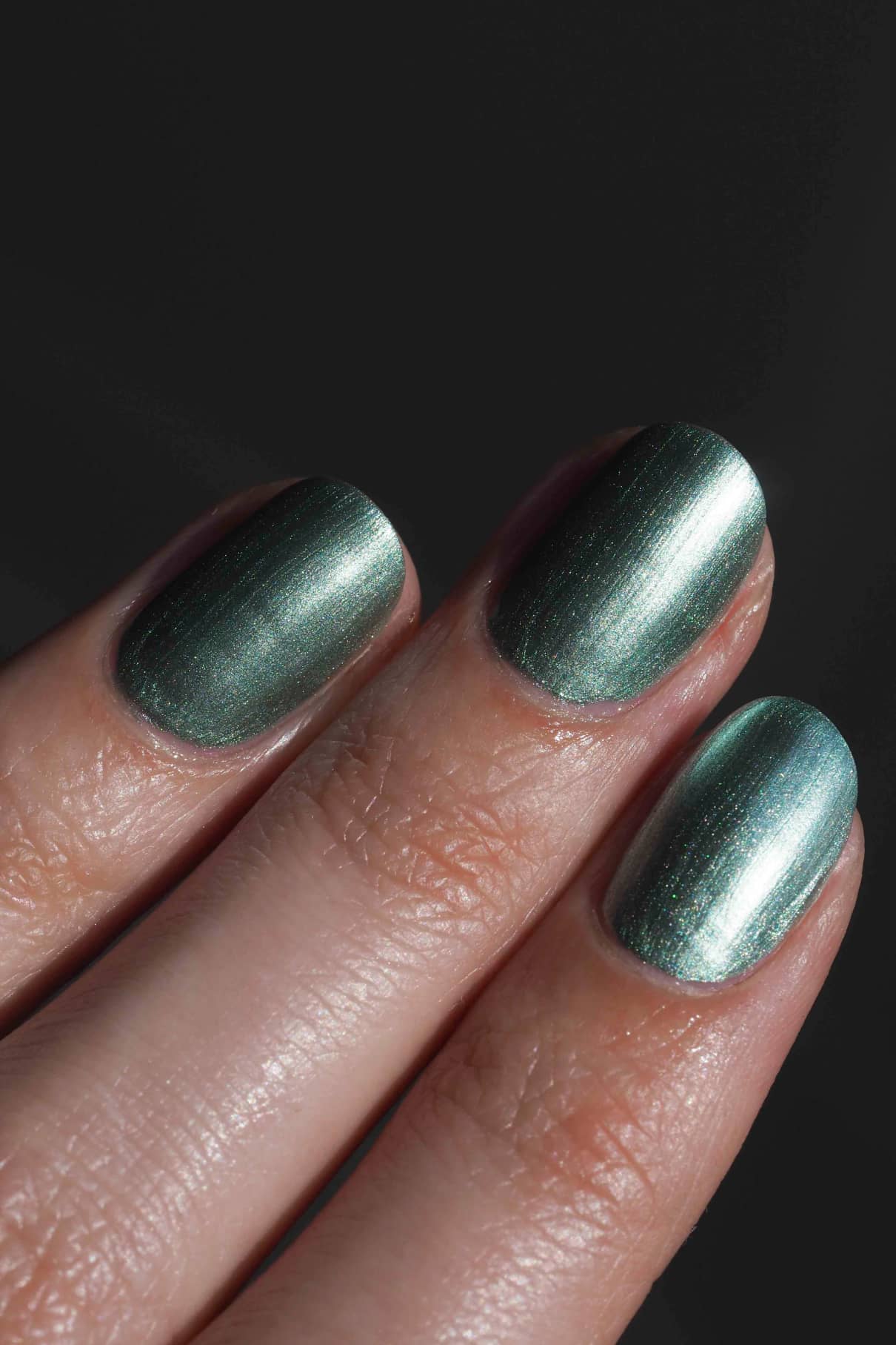 Eine Nahaufnahme von drei Fingernägeln, die mit gitti no. 305, einem metallisch grünen Nagellack in einem ruhigen Ton, vor einem dunklen Hintergrund.