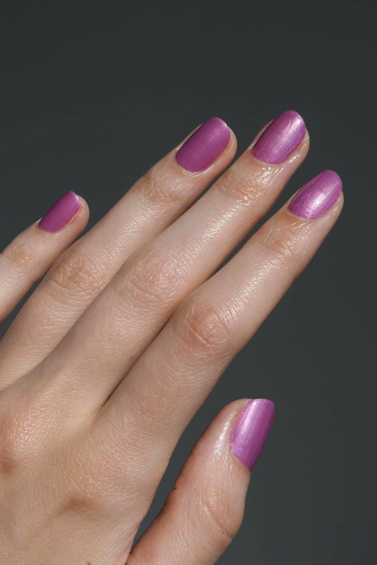 Eine Hand mit sauber manikürten Nägeln, lackiert in gitti no. 306, einem Metallic-Mauve-Ton mit violettem Unterton, vor einem schlichten dunklen Hintergrund.